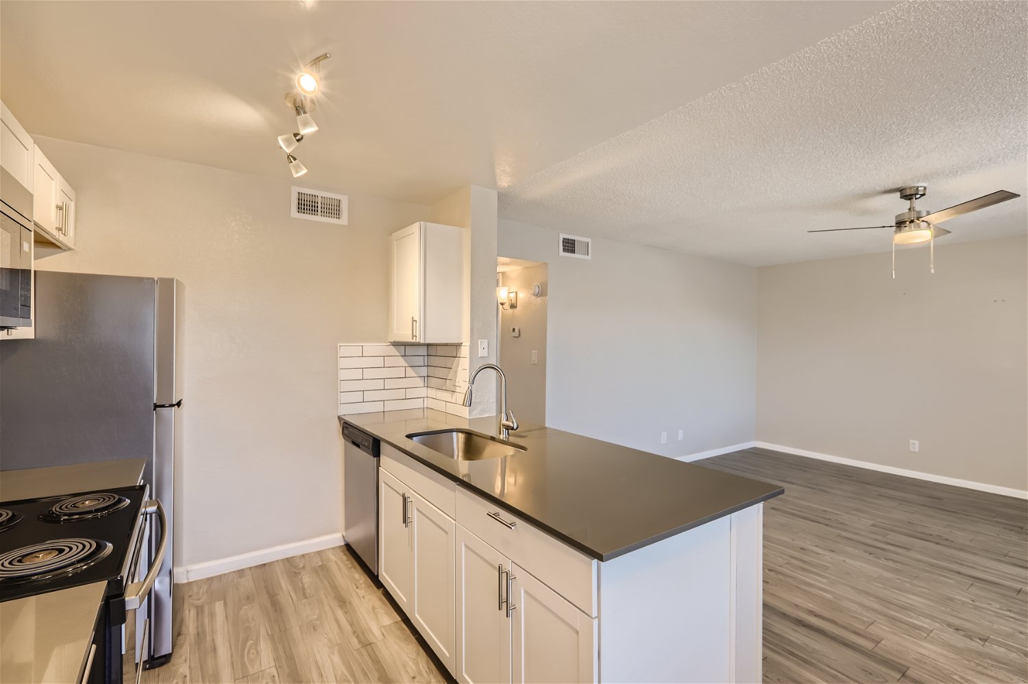 A kitchen with stainless steel appliances, grey quartz countertops and the living room at Rise Trail