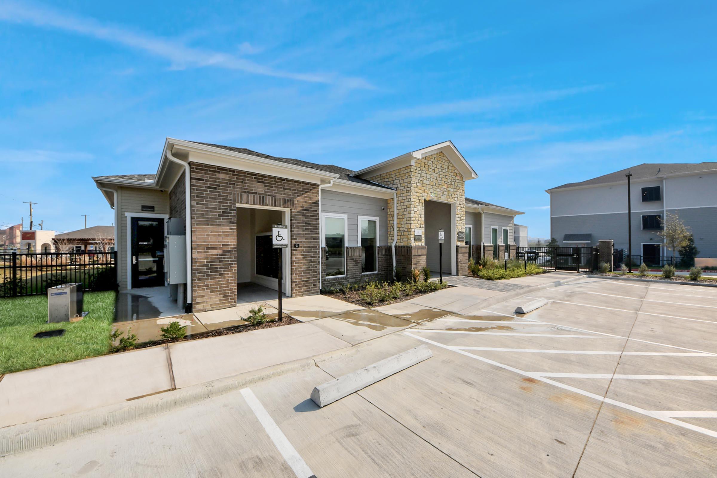 A modern one-story building featuring a combination of brick and stone exterior, with landscaped areas and accessible parking. The building has large windows and a welcoming entrance. Adjacent to the structure is a paved parking lot with clearly marked spaces. The sky is clear and blue.