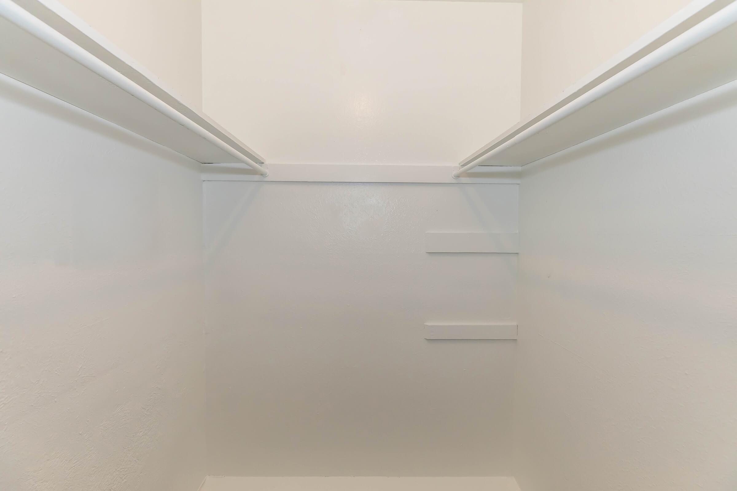 Empty closet interior with white walls and two horizontal rods for hanging clothes. The space appears clean and unadorned, with a couple of built-in shelves on the back wall. Ideal for storage or organization purposes.