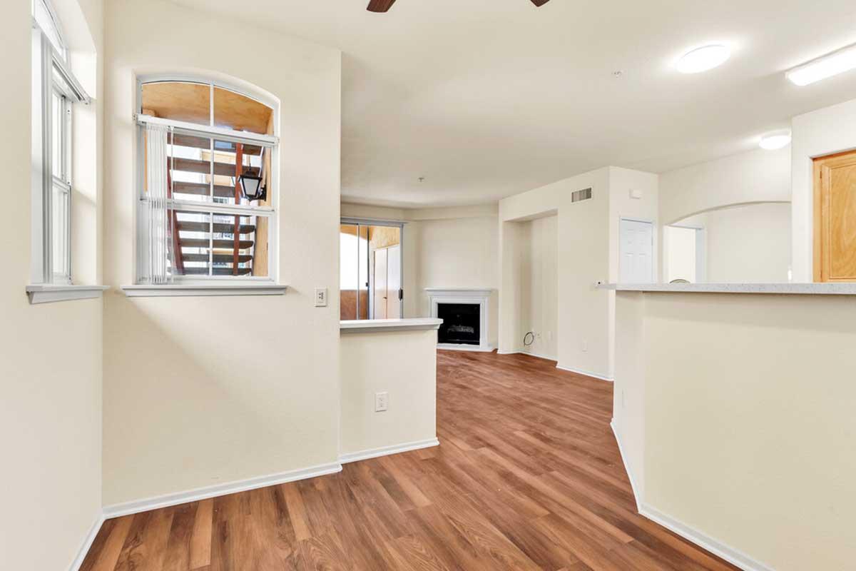 A spacious interior view of a modern living area featuring wooden flooring, a fireplace, and large windows. Light-colored walls and an open layout create a bright atmosphere. A staircase is visible in the background, leading to an upper level.