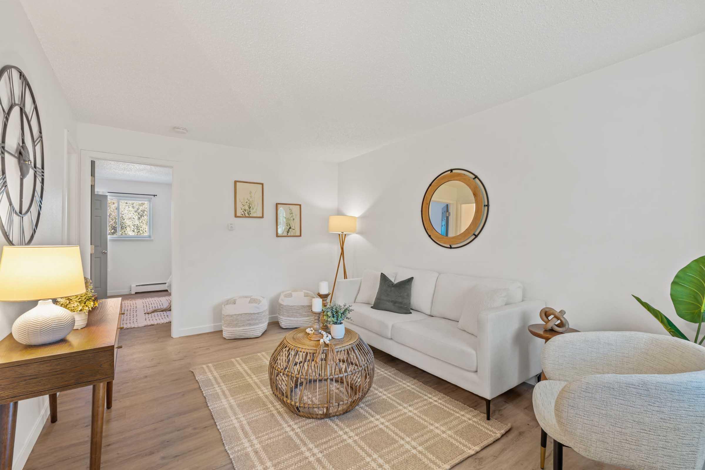 A cozy living room featuring a light-colored sofa, round mirror on the wall, a wooden coffee table with decorative items, and a floor lamp. The space is accented with woven baskets for storage and a soft area rug, creating a welcoming and modern atmosphere. Greenery adds a touch of nature.
