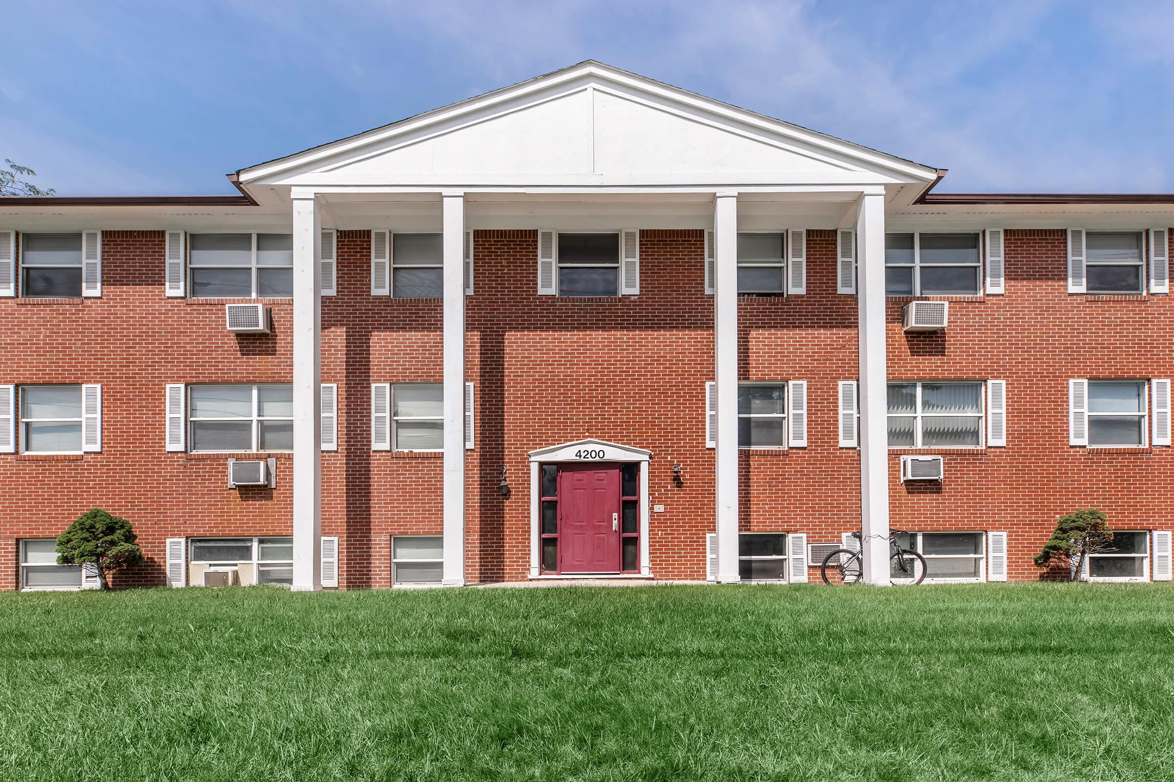 a large brick building with grass in front of a house with Grinter Place in the background