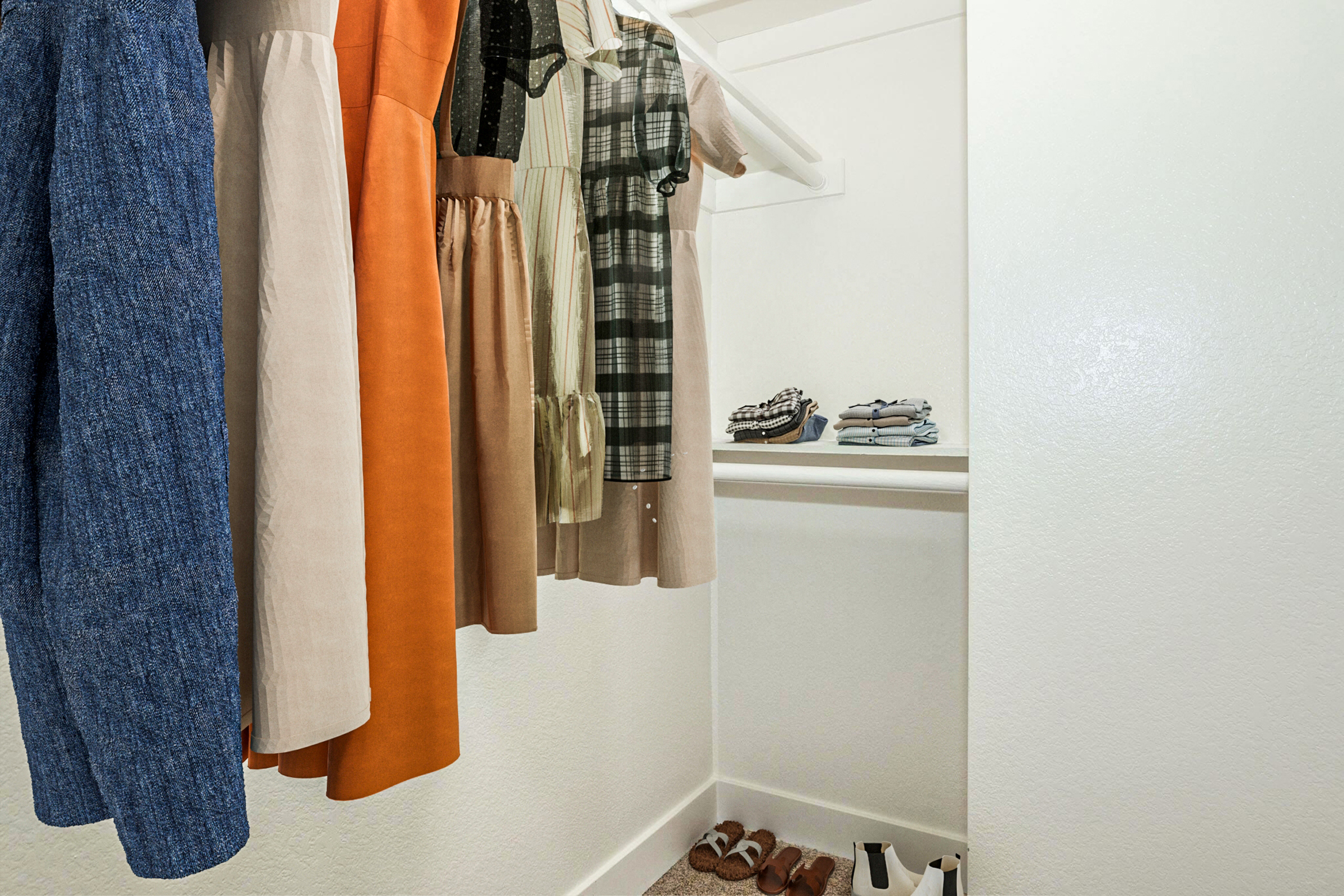 A neatly organized closet showcasing a variety of women's clothing. The clothes include dresses in different colors and styles hanging on a rack, and neatly folded items on a shelf below. A pair of sandals and heels are visible on the floor, adding a touch of personal styling to the space.