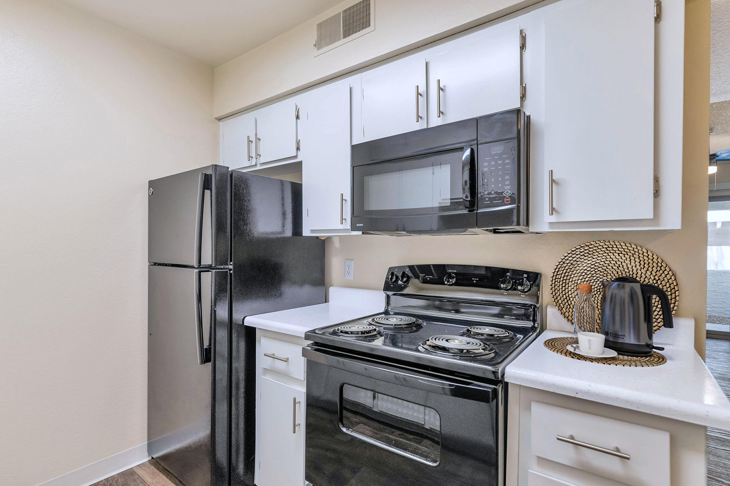 Modern kitchen featuring white cabinets, black appliances including a refrigerator and an oven with a stovetop. A microwave is mounted above the stove, and a decorative woven basket sits next to a coffee maker on the countertop. Soft neutral walls complete the inviting ambiance.