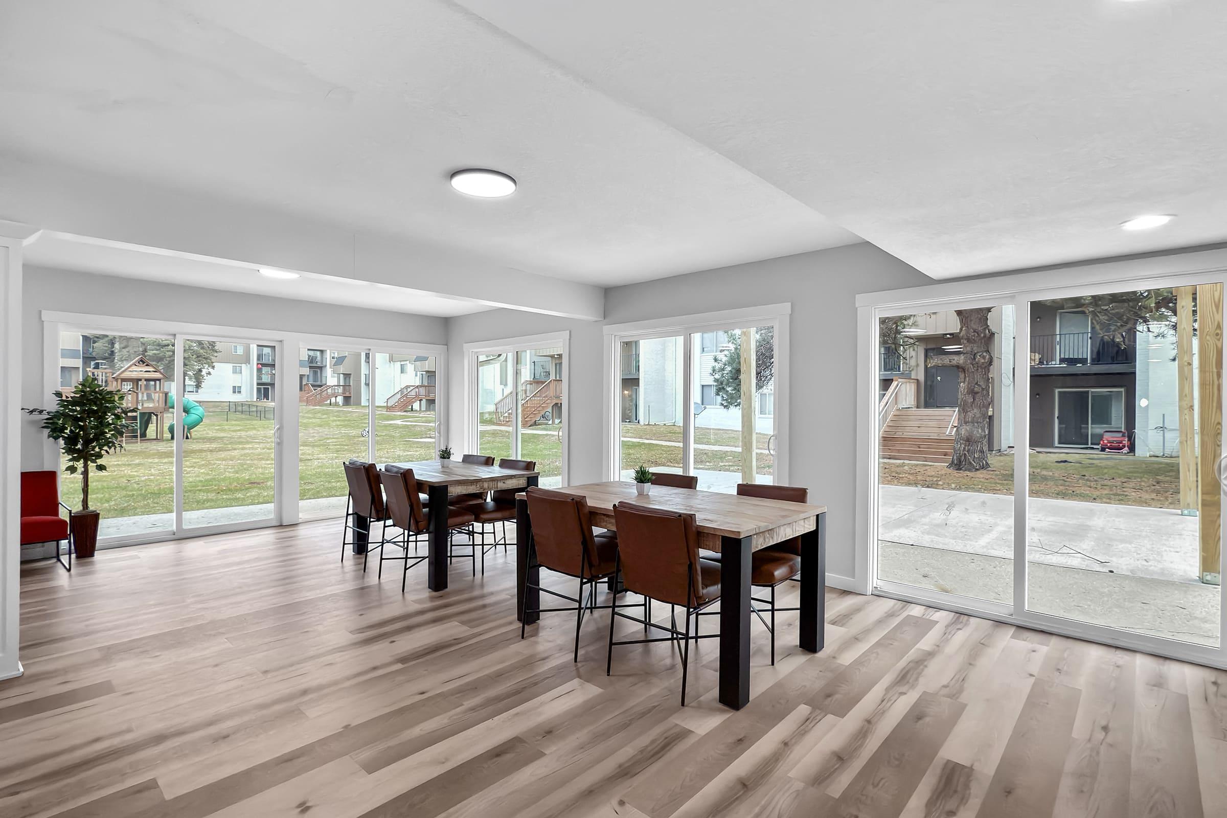 Bright, modern dining area featuring a large table with chairs, set against a backdrop of sliding glass doors. Natural light floods the space, highlighting the wood flooring and neutral walls. Outside, a grassy area and playground are visible, enhancing the open feel of the room.