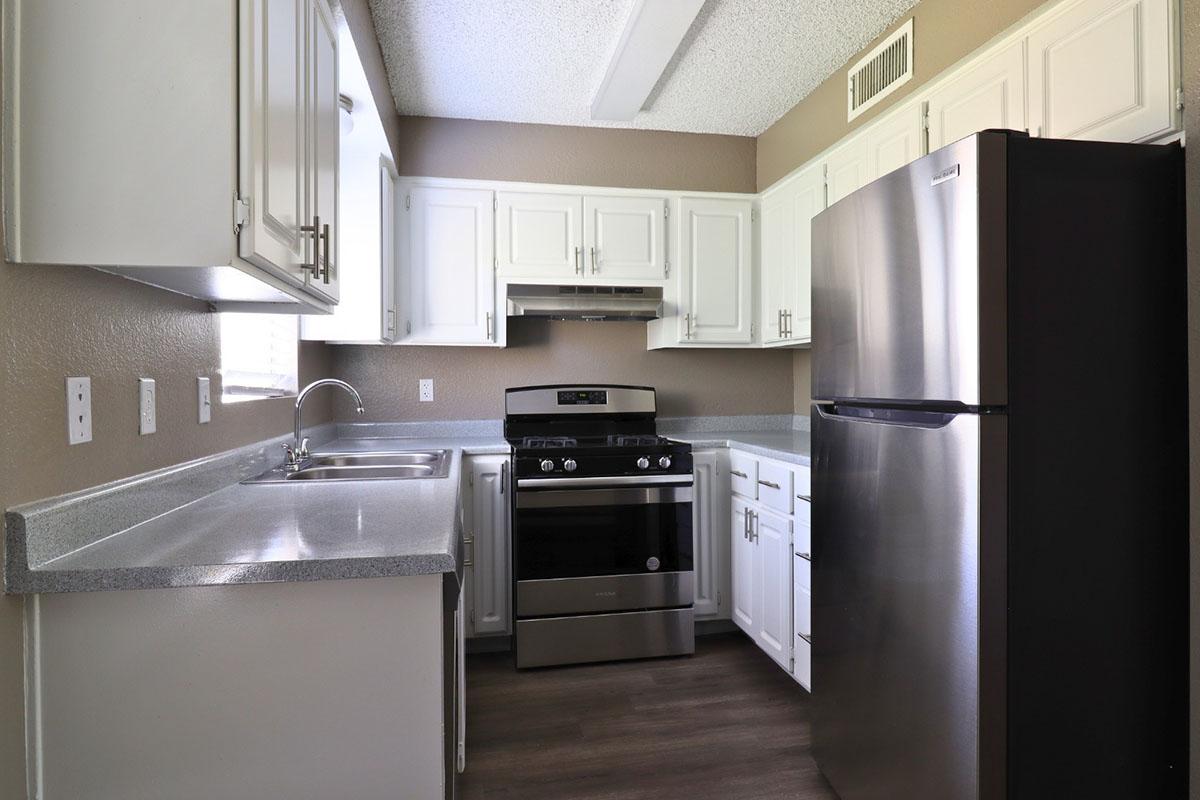 Modern kitchen featuring white cabinets, a stainless steel refrigerator, and a gas stove with an overhead microwave. Countertops are gray, and the space is well-lit with natural light coming through a window. The flooring is dark, providing a contemporary contrast to the cabinetry.