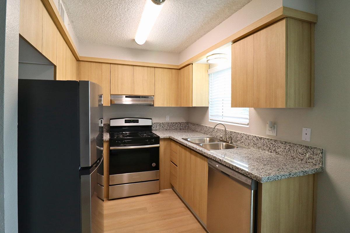 Modern kitchen featuring light wood cabinetry, stainless steel appliances, and granite countertops. Includes a black oven, silver dishwasher, and double sink under a window with natural light. The flooring is a light wood laminate, creating a warm and inviting atmosphere.