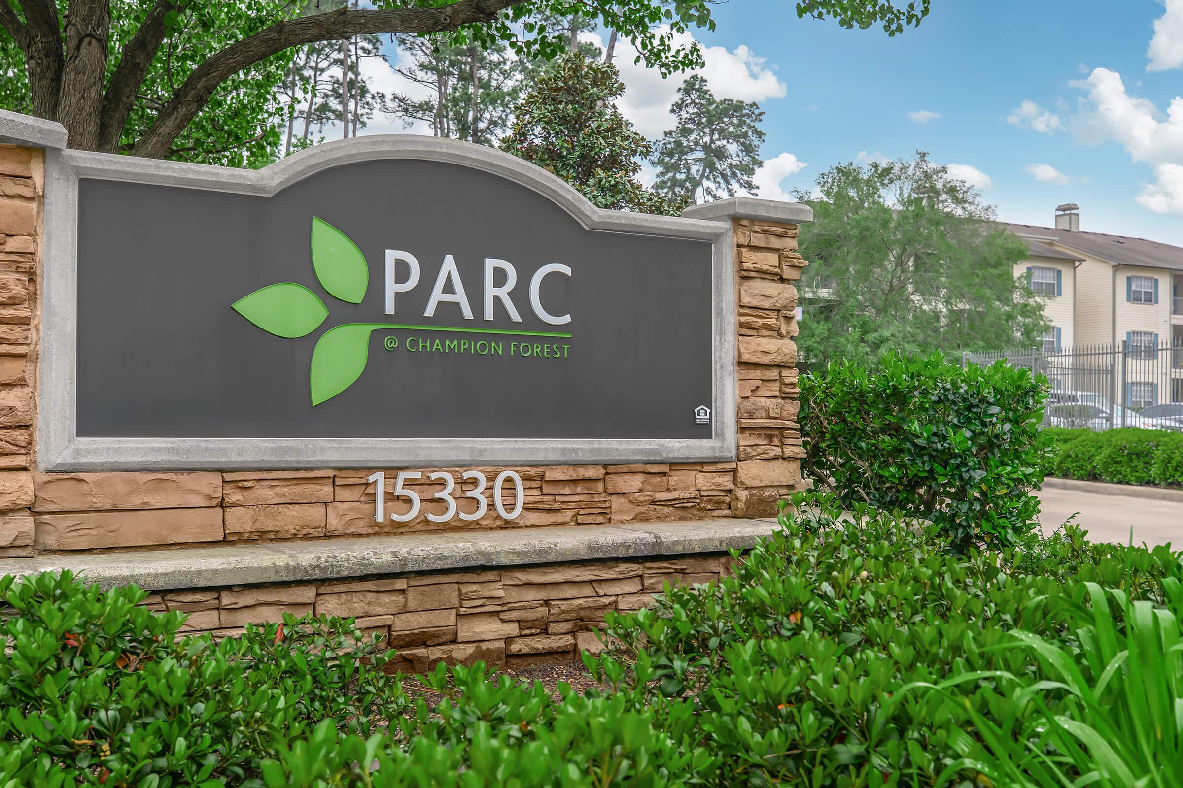Sign for PARC at Champion Forest, featuring a green logo with leaves and the address "15330." Surrounding greenery adds a welcoming touch to the entrance.