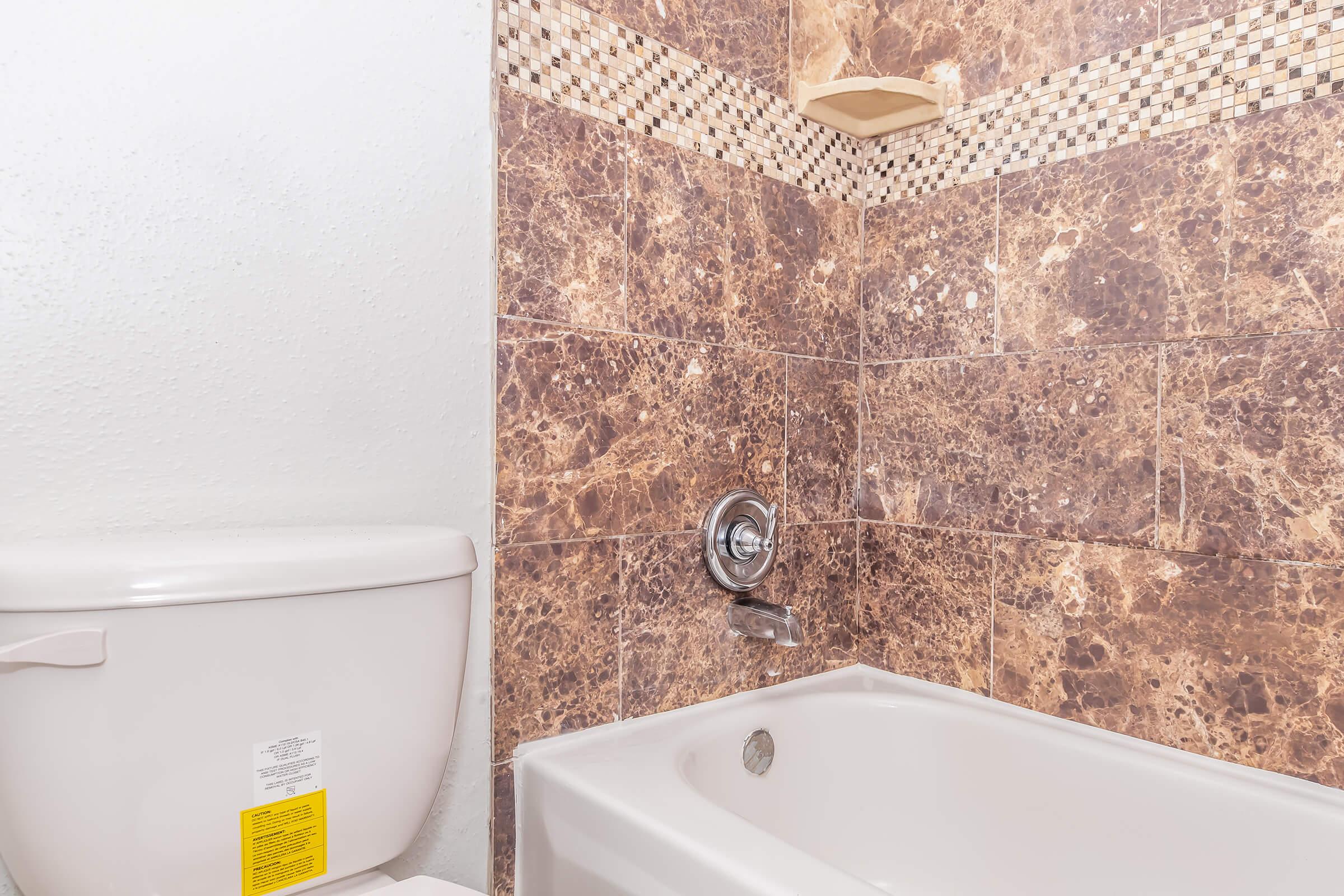 A view of a bathroom featuring a white toilet and a bathtub with a chrome faucet. The walls are decorated with shiny brown marble tiles, adding a modern touch to the space. There is a small shelf above the bathtub, designed for storage or decor.