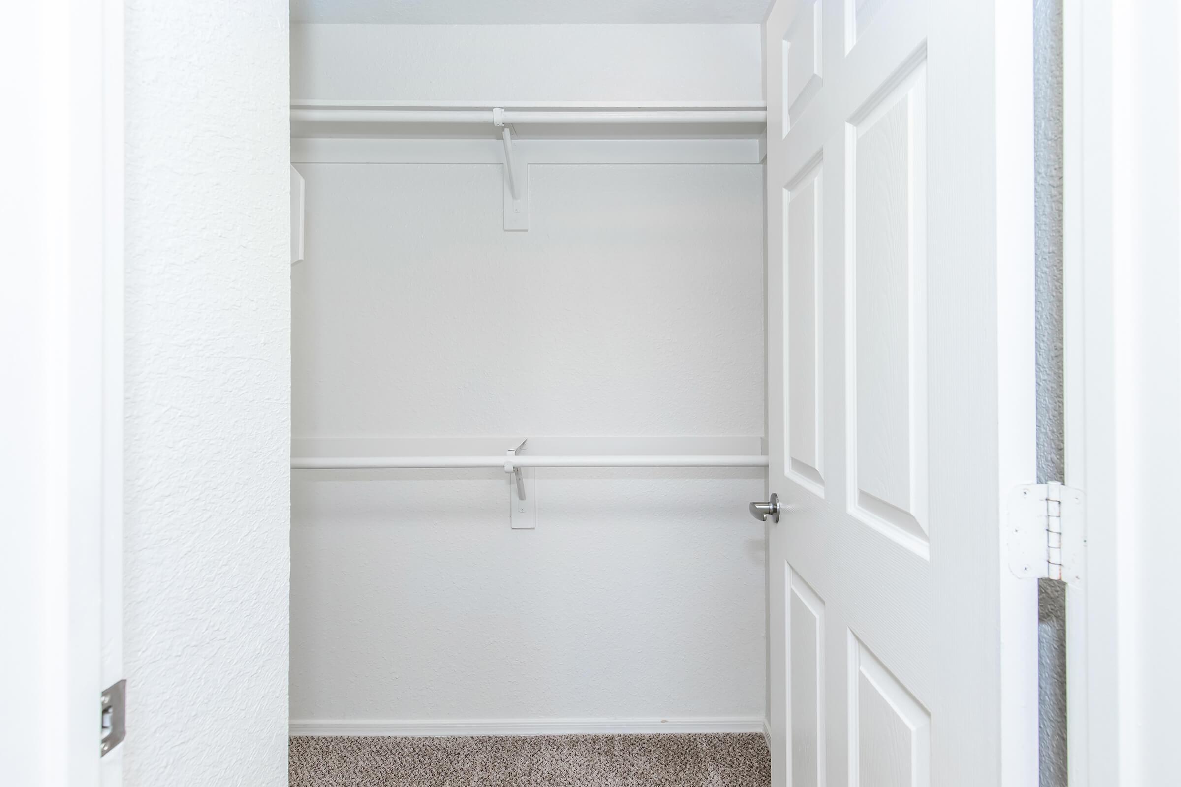 Empty closet with white walls and a carpeted floor. The two doors are open, revealing a simple, organized space with a hanging rod and no shelves. The interior looks clean and minimalistic, suitable for storage or organization.