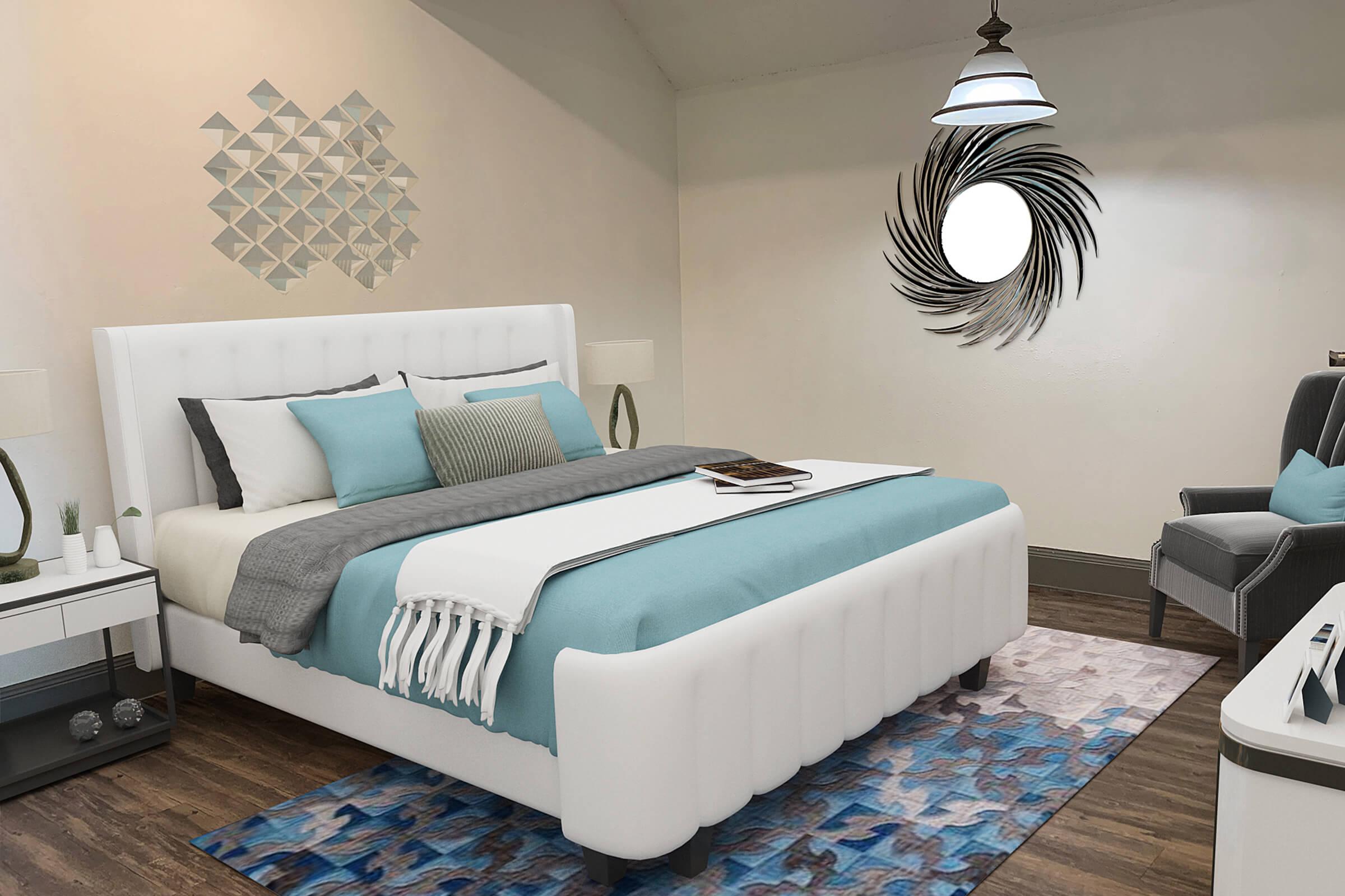 A well-decorated bedroom featuring a white upholstered bed with blue and gray bedding, a modern rug with abstract patterns, a stylish round mirror on the wall, and a geometric wall art piece. There are two bedside lamps, a small nightstand, and an armchair to create a cozy atmosphere.