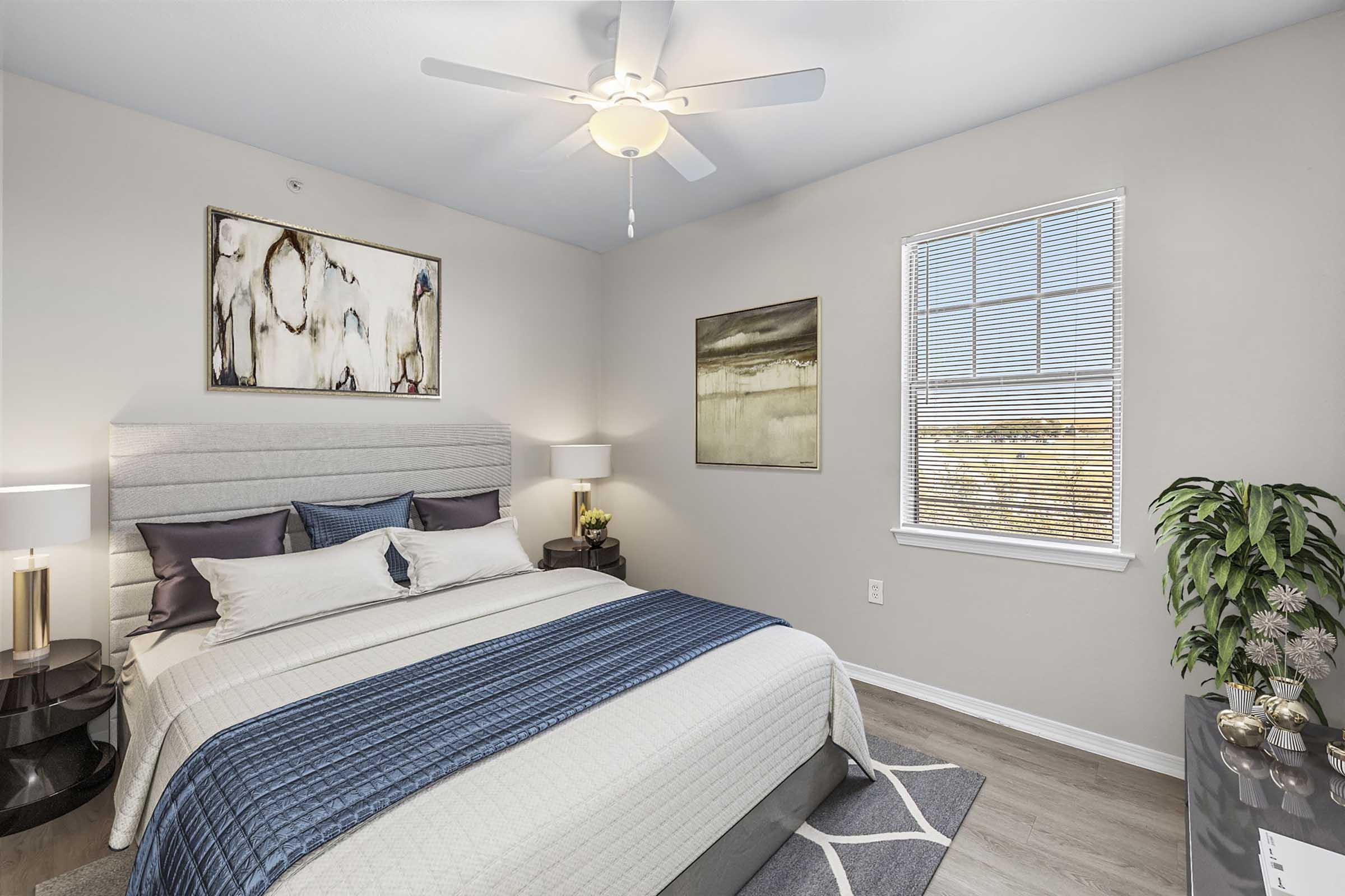 A modern bedroom featuring a neatly made bed with blue and white bedding, flanked by two contemporary nightstands with lamps. There are two framed artworks on the light-colored walls, a window allowing natural light, and a green potted plant in the corner, enhancing the room's inviting atmosphere.