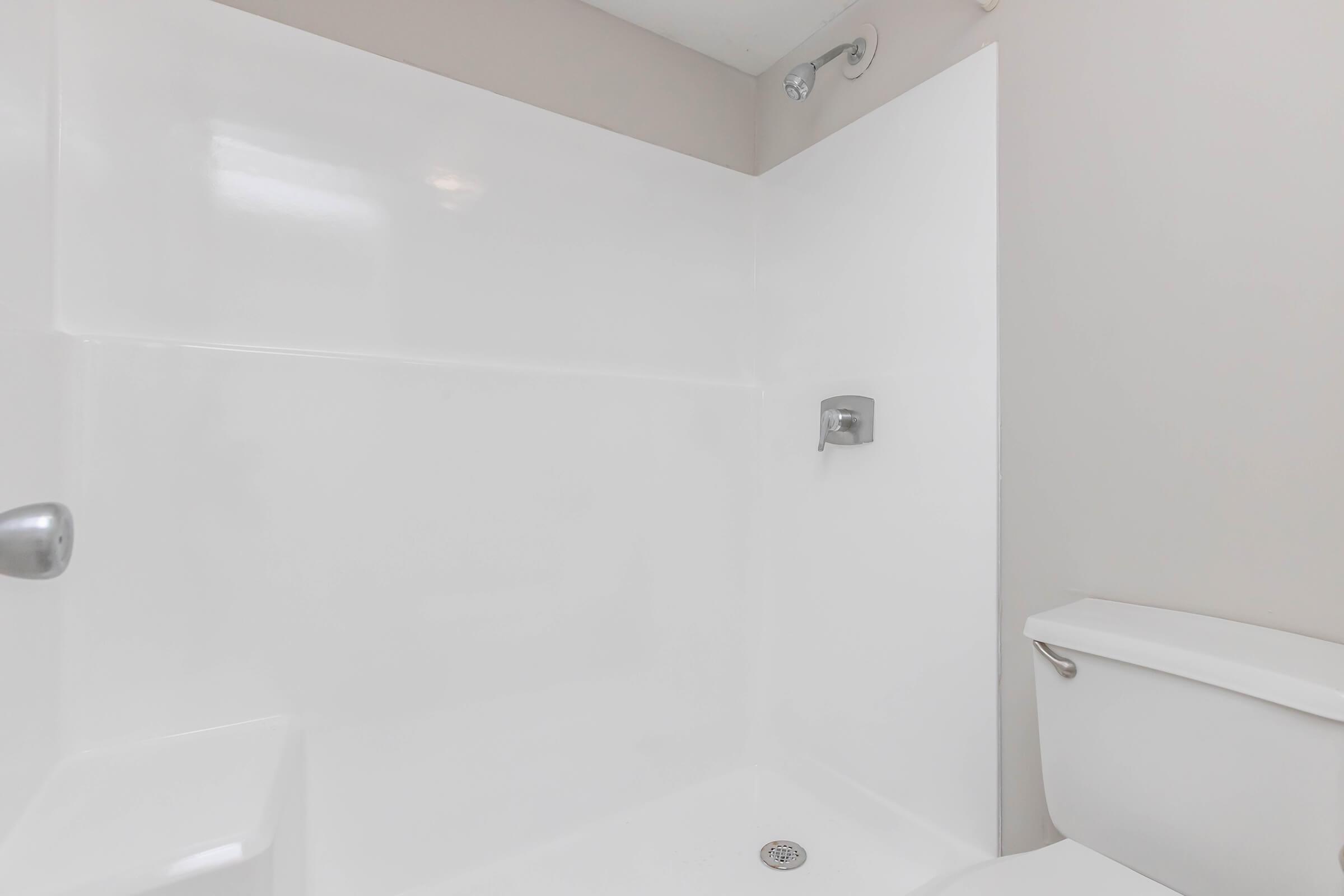 A clean, modern bathroom featuring a white bathtub and shower area, with smooth walls and a showerhead mounted on the wall. A toilet is visible in the corner, completing the space. The overall aesthetic is bright and simple, emphasizing hygiene and functionality.