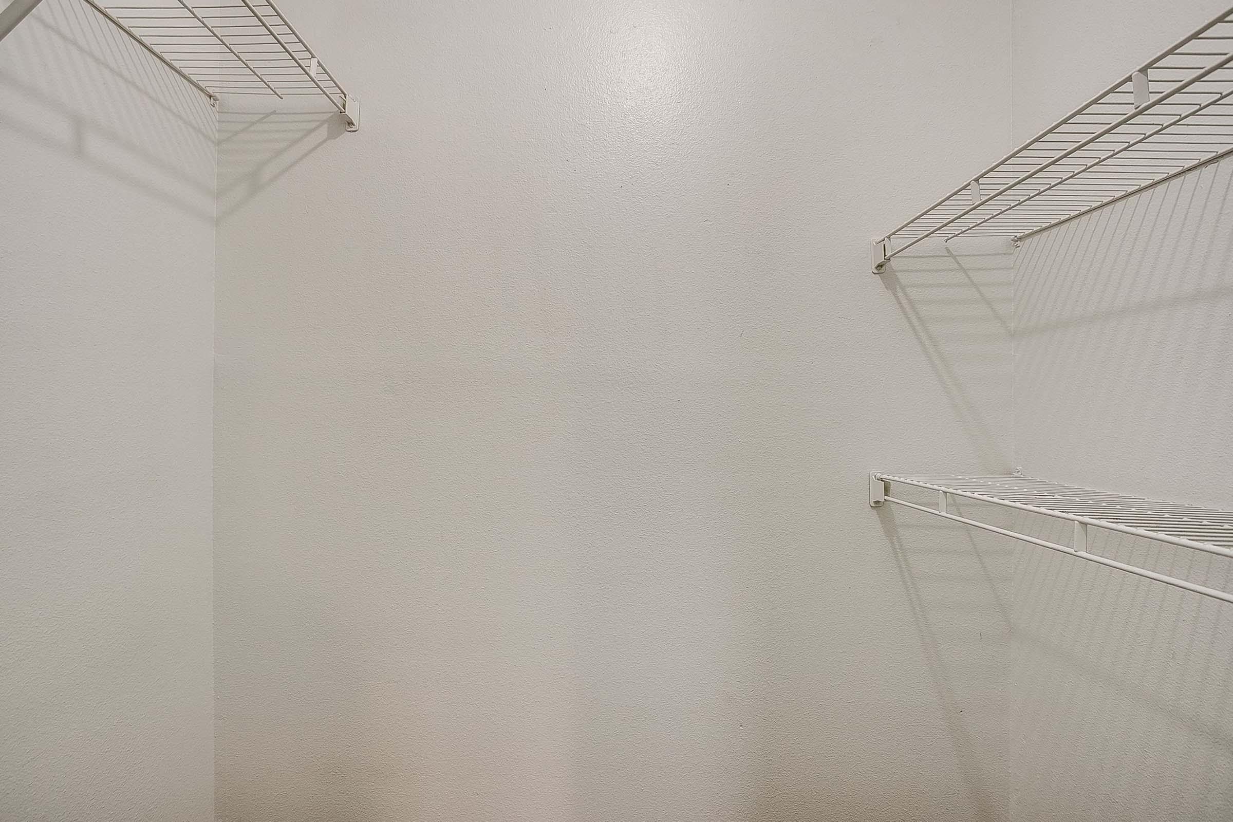 Empty closet with white walls and wire shelving. The space is bright and uncluttered, featuring two shelves on the left and one on the right. The lack of items gives it a clean, spacious appearance.