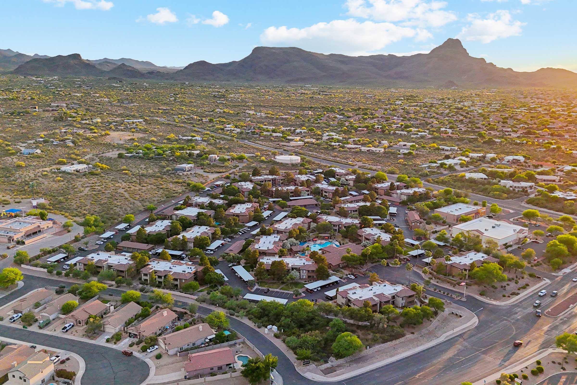 Aerial view of a residential area with a mix of single-story homes and multi-story buildings, surrounded by arid landscape and mountains in the background.