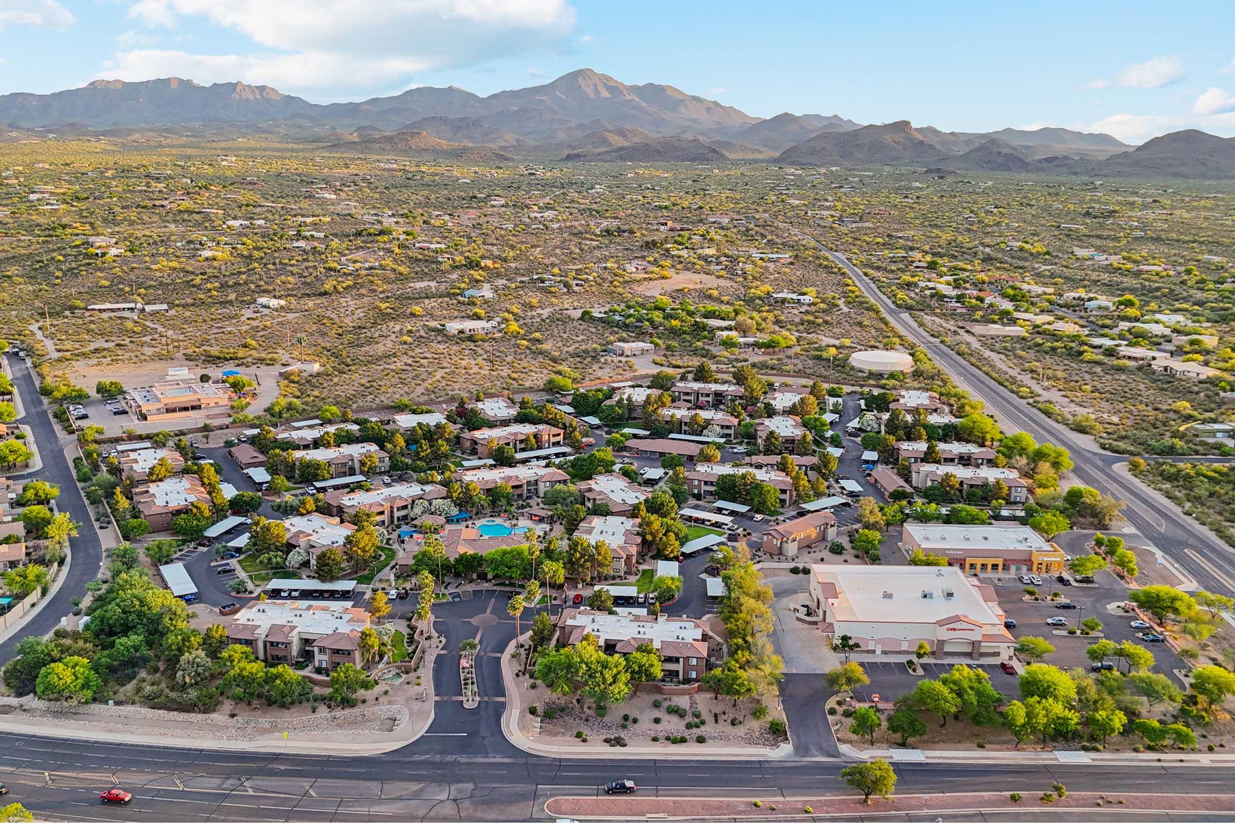 Aerial view of a suburban neighborhood surrounded by mountains, featuring well-organized residential buildings, a swimming pool, landscaping with trees, and roads.