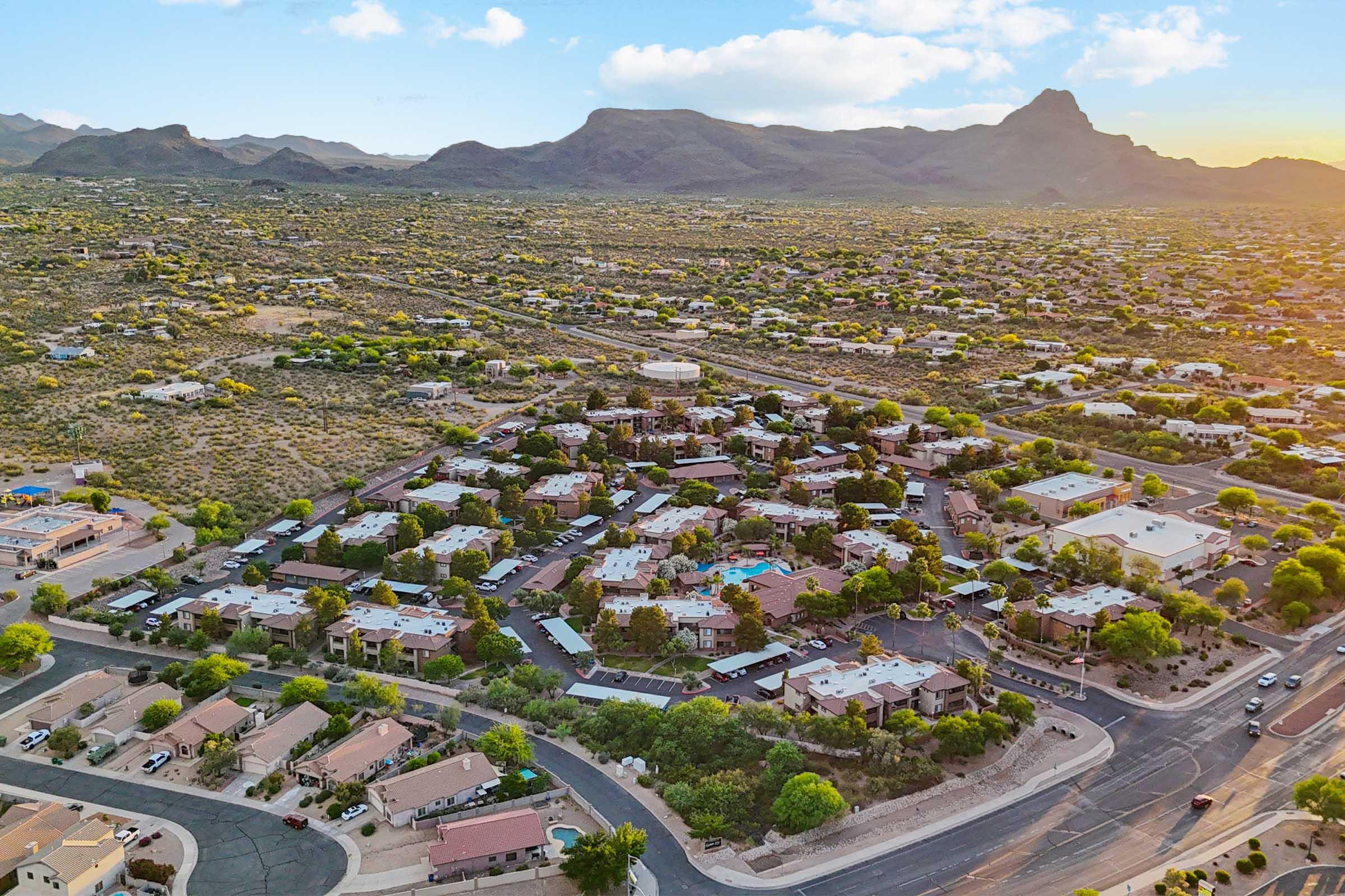 Aerial view of a residential neighborhood with a mix of houses and low-rise buildings surrounded by arid landscape and mountains in the background.