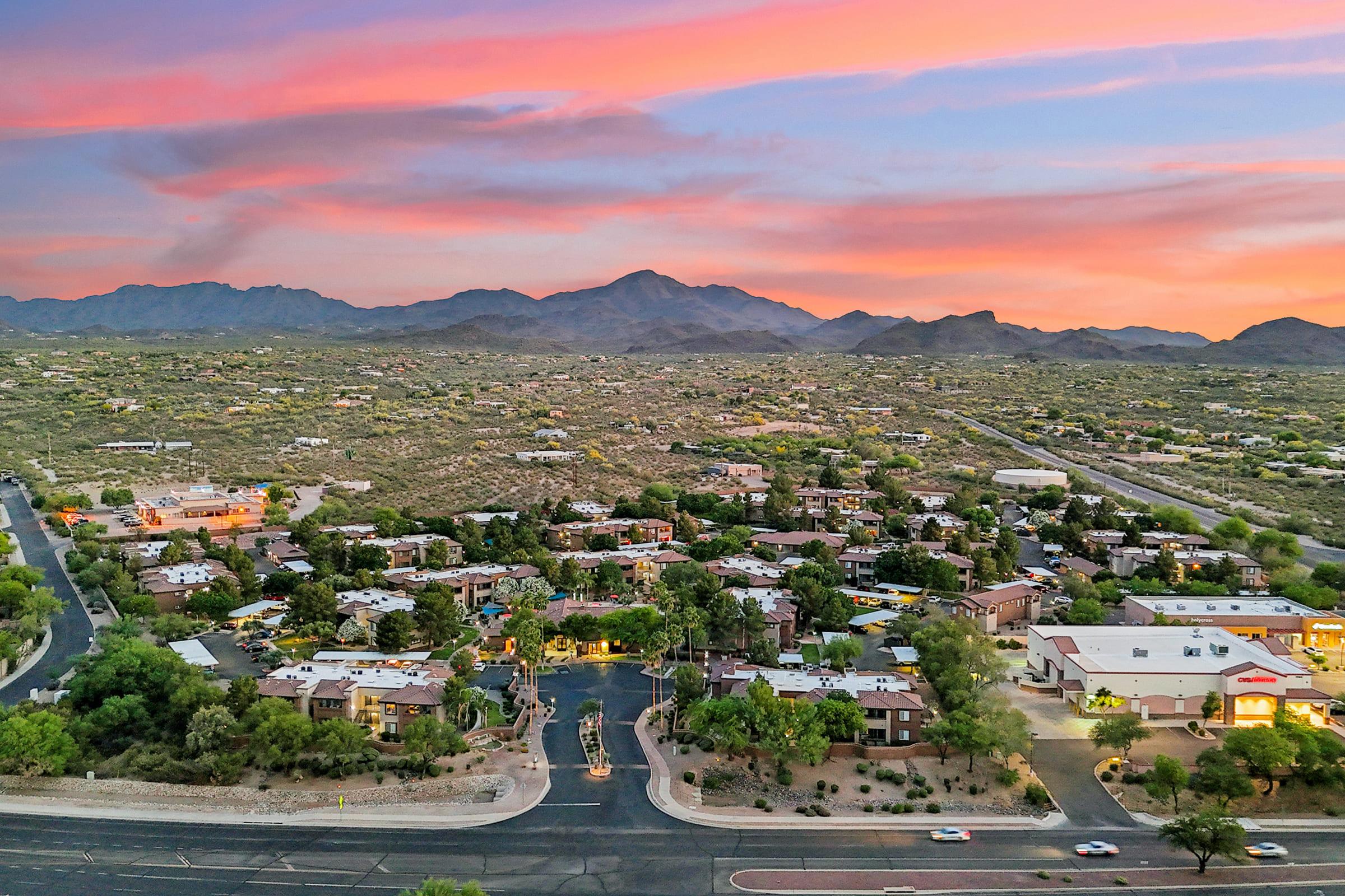 Aerial view of a desert landscape at sunset, featuring a small community with residential buildings surrounded by mountains.