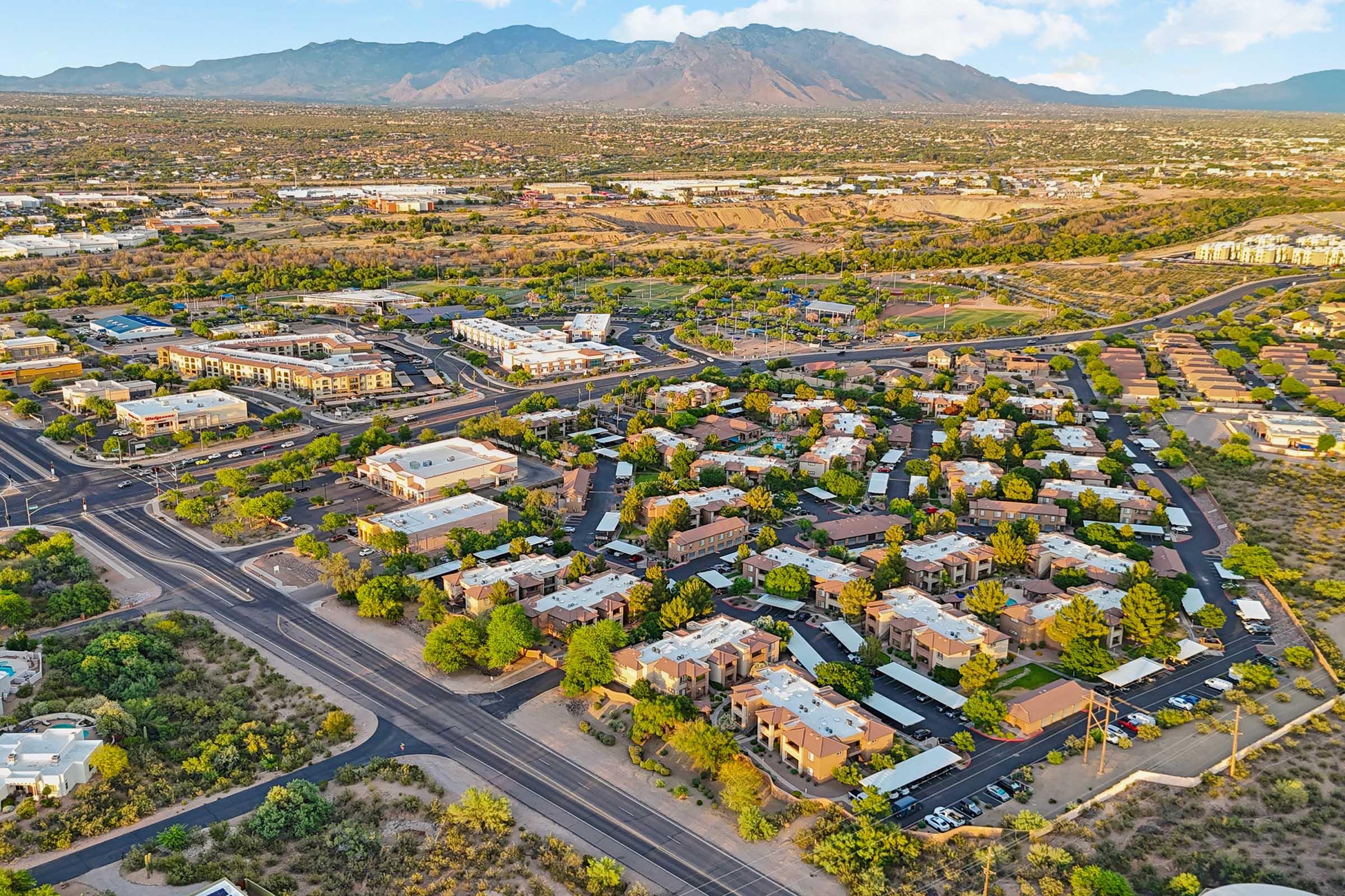 An aerial view of a suburban neighborhood with winding roads, clusters of houses, and greenery, set against a backdrop of mountains.