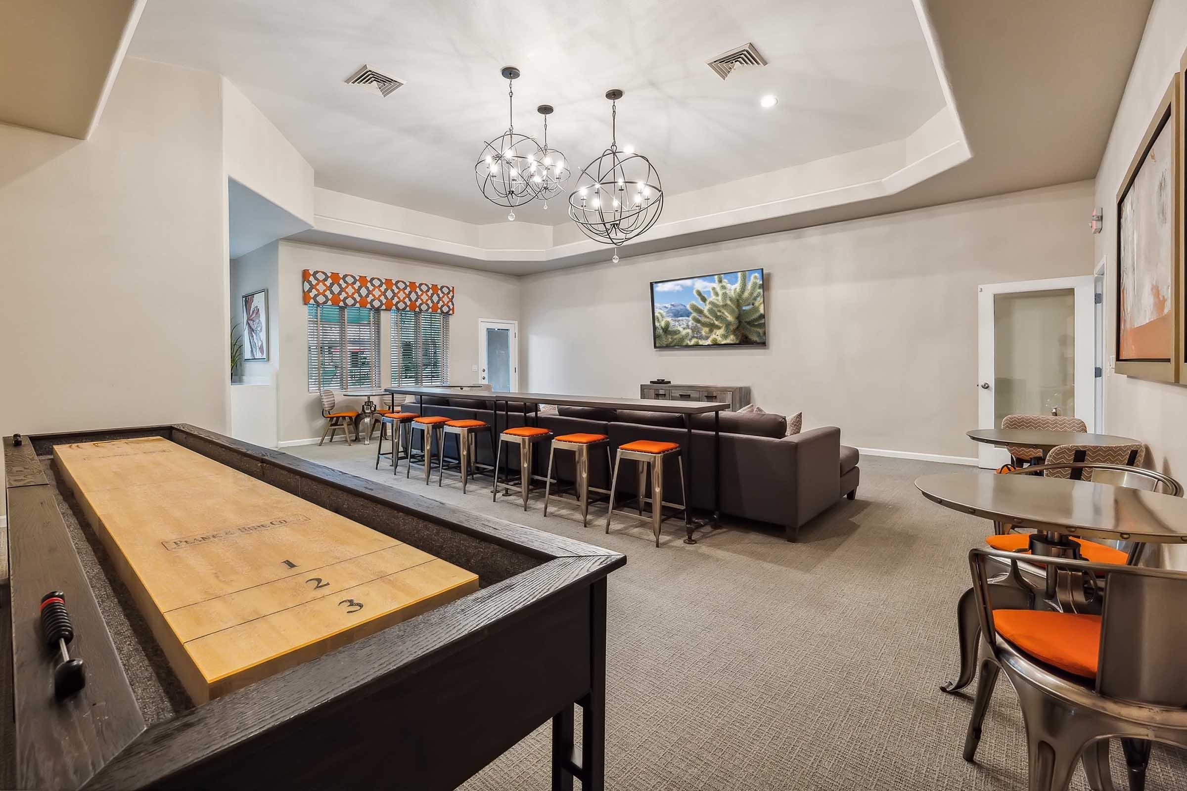 A spacious lounge area featuring a shuffleboard table, modern seating, and a large TV mounted on the wall.