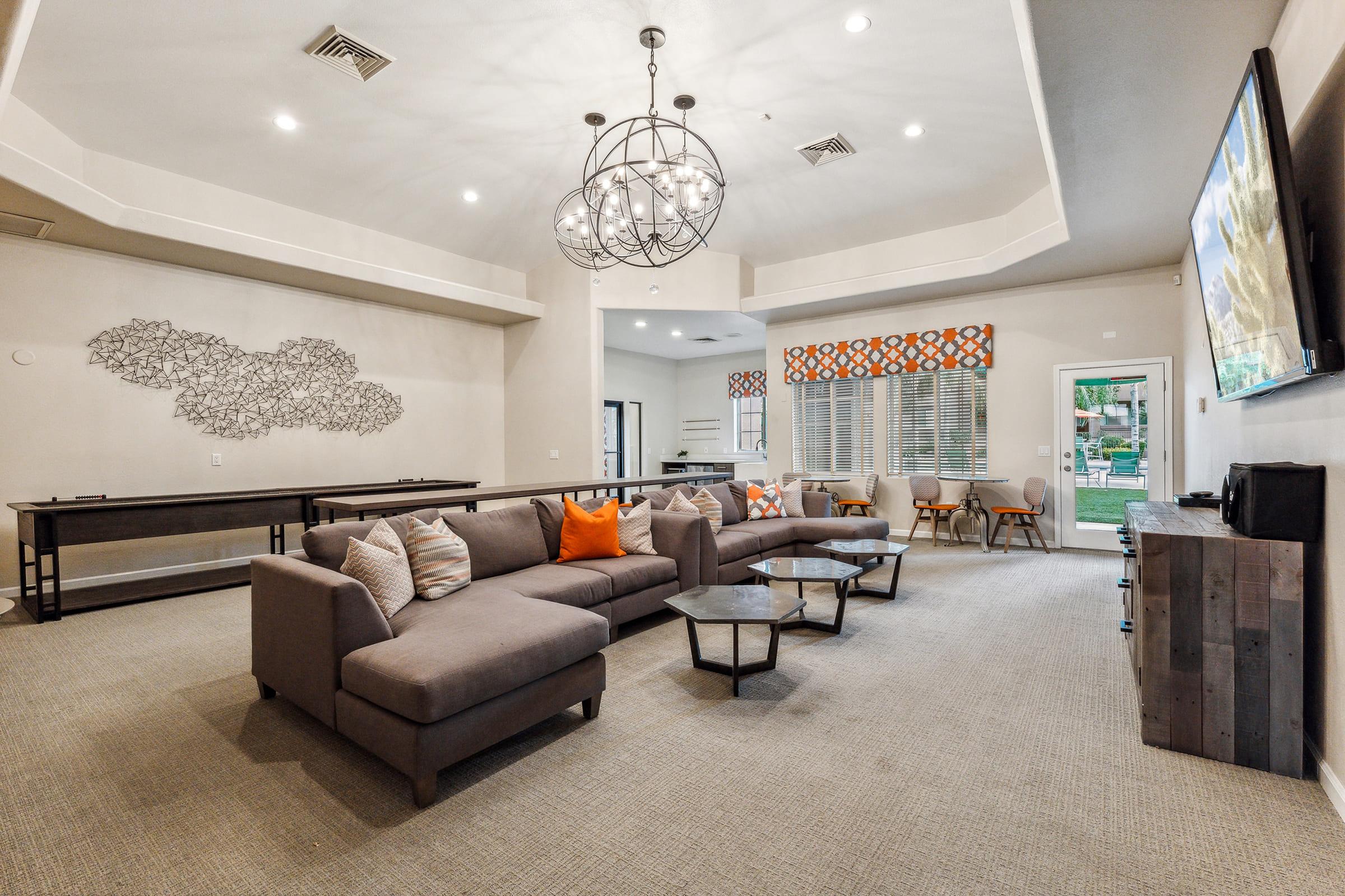 A modern living room featuring a large sectional sofa with decorative pillows, two stylish coffee tables, a contemporary chandelier, and a flat-screen TV.