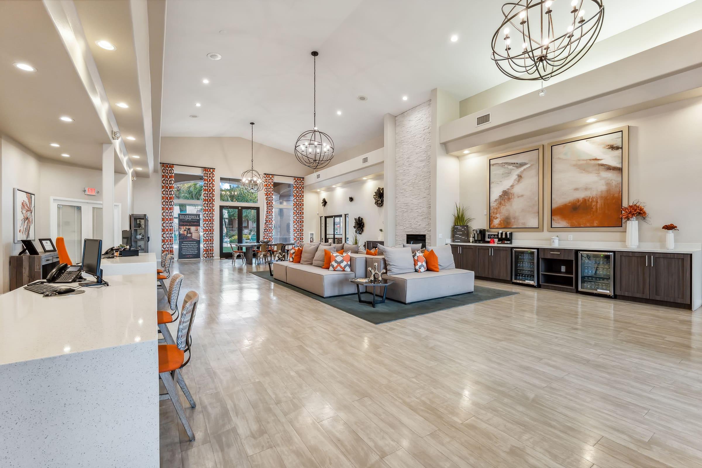 A spacious lobby area featuring modern decor with a large seating arrangement, decorative artwork on the walls, large windows allowing natural light, and a reception desk.