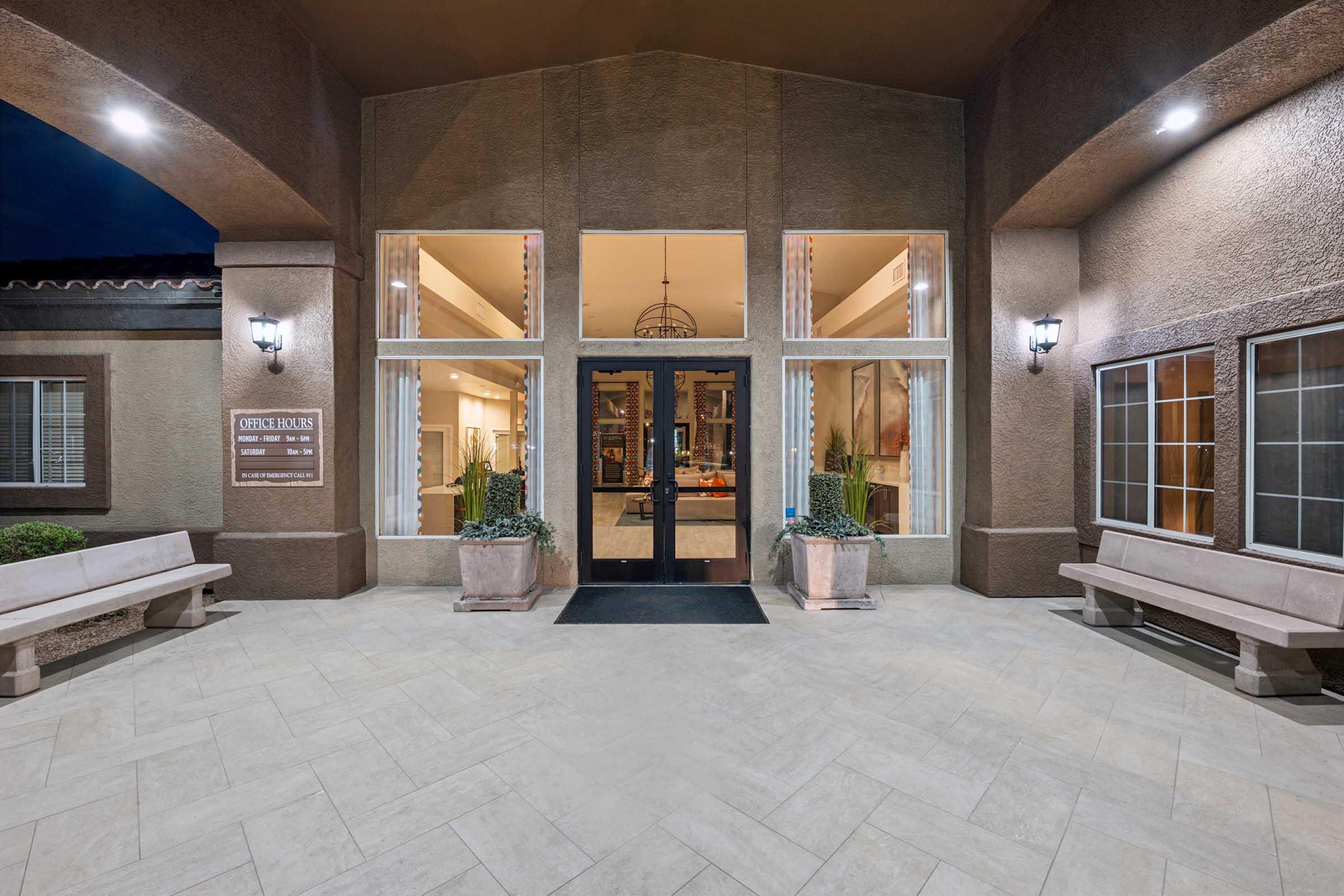 Front entrance of a building with large glass double doors, flanked by two benches.