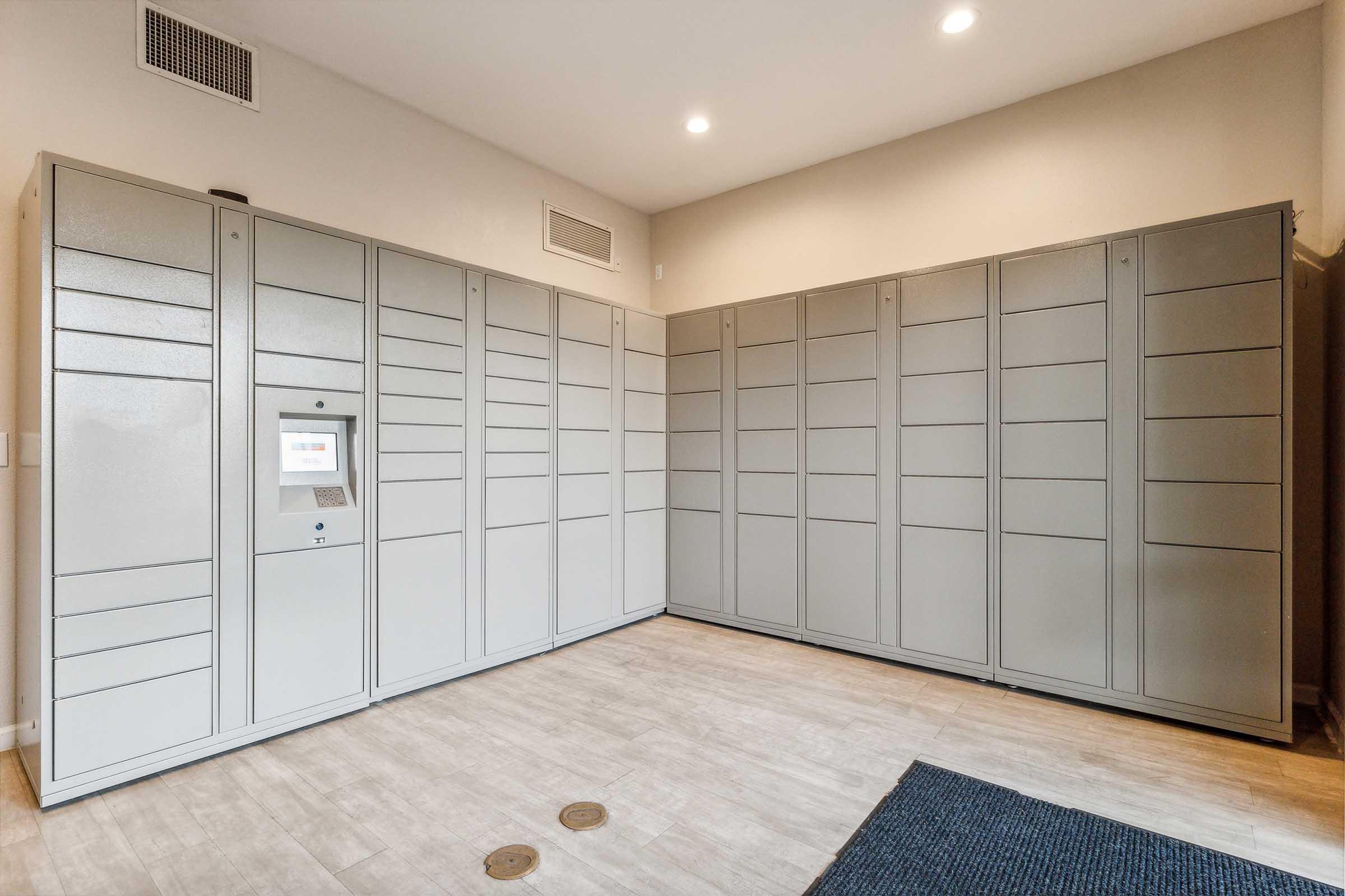 A room featuring multiple gray delivery lockers arranged against the walls.