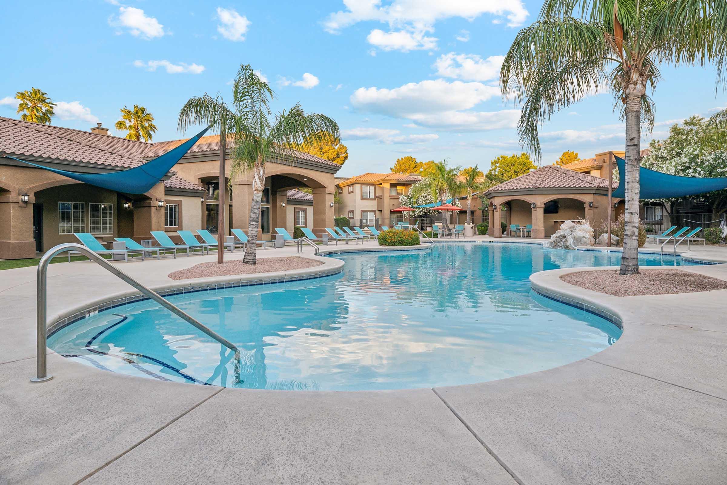 A sparkling outdoor pool surrounded by palm trees and lounge chairs.
