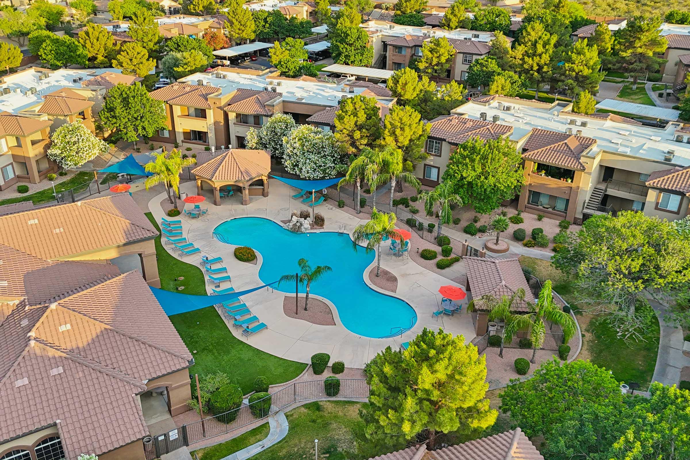 Aerial view of a residential complex featuring a swimming pool surrounded by lounge chairs and palm trees.