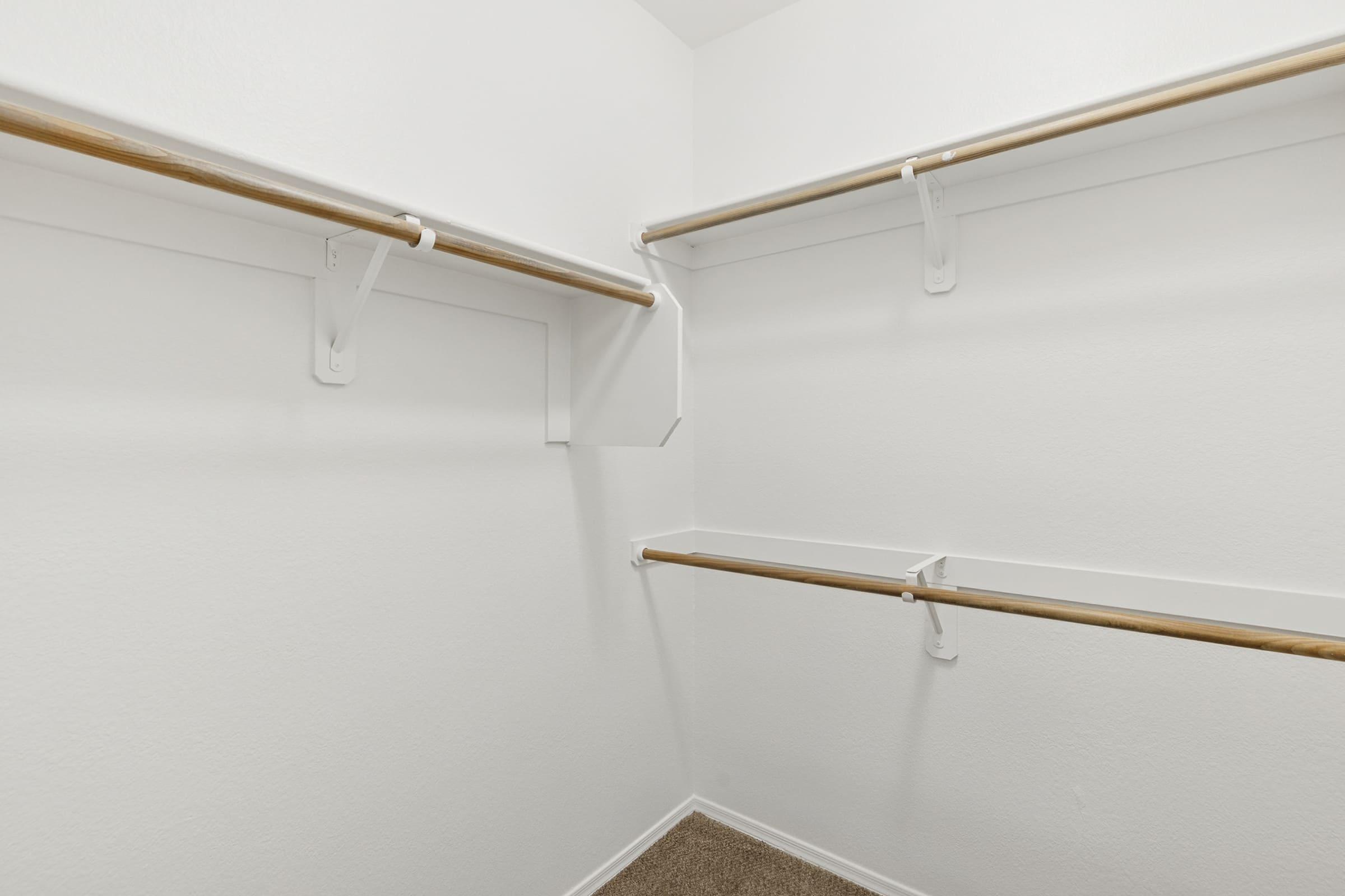 Empty walk-in closet featuring white walls and a tan carpet. Two wooden clothes rods are mounted on the walls, with a small shelf in the corner, indicating a minimalistic and organized storage space.