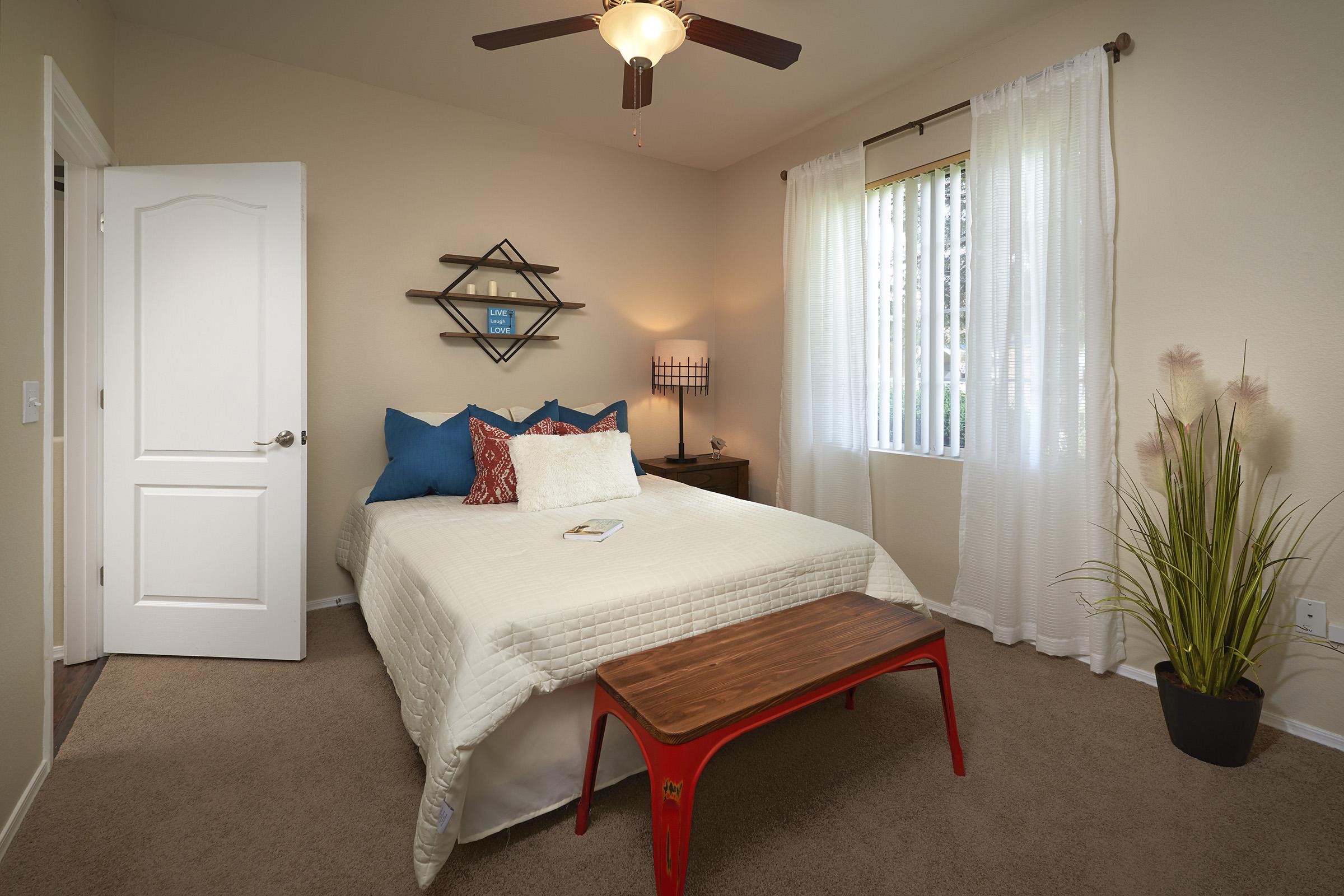 A cozy bedroom featuring a white bed with decorative pillows, a small wooden bench at the foot, and a bedside table.