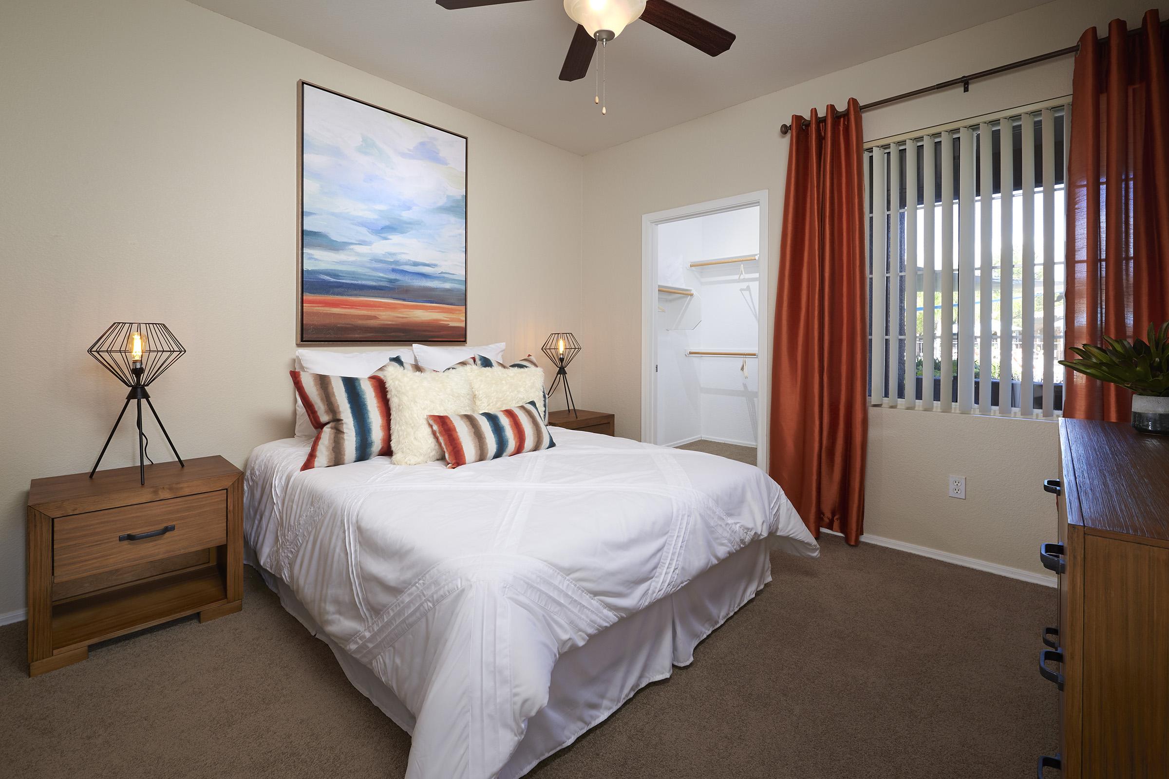 A cozy bedroom featuring a queen-sized bed with decorative pillows, a piece of abstract art above the bed, and two stylish bedside lamps.