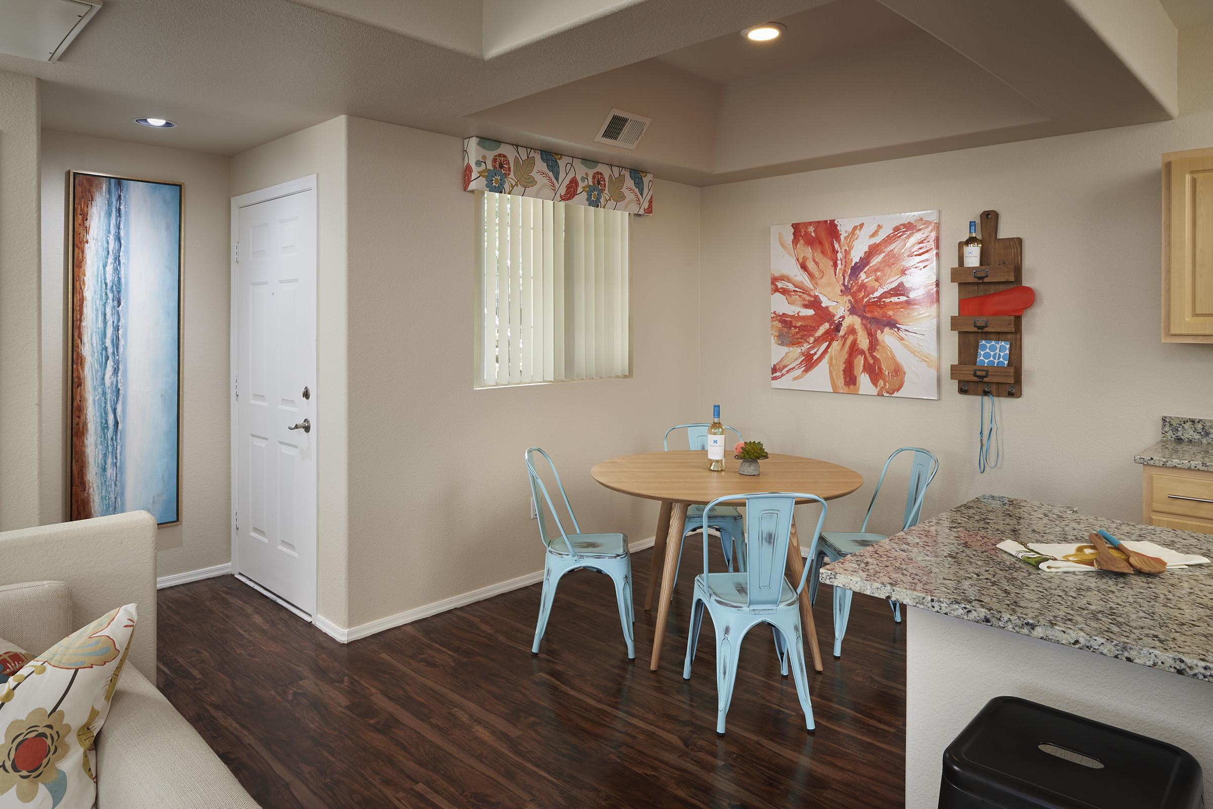 A modern, well-lit kitchen and dining area featuring a round wooden table surrounded by light blue chairs.