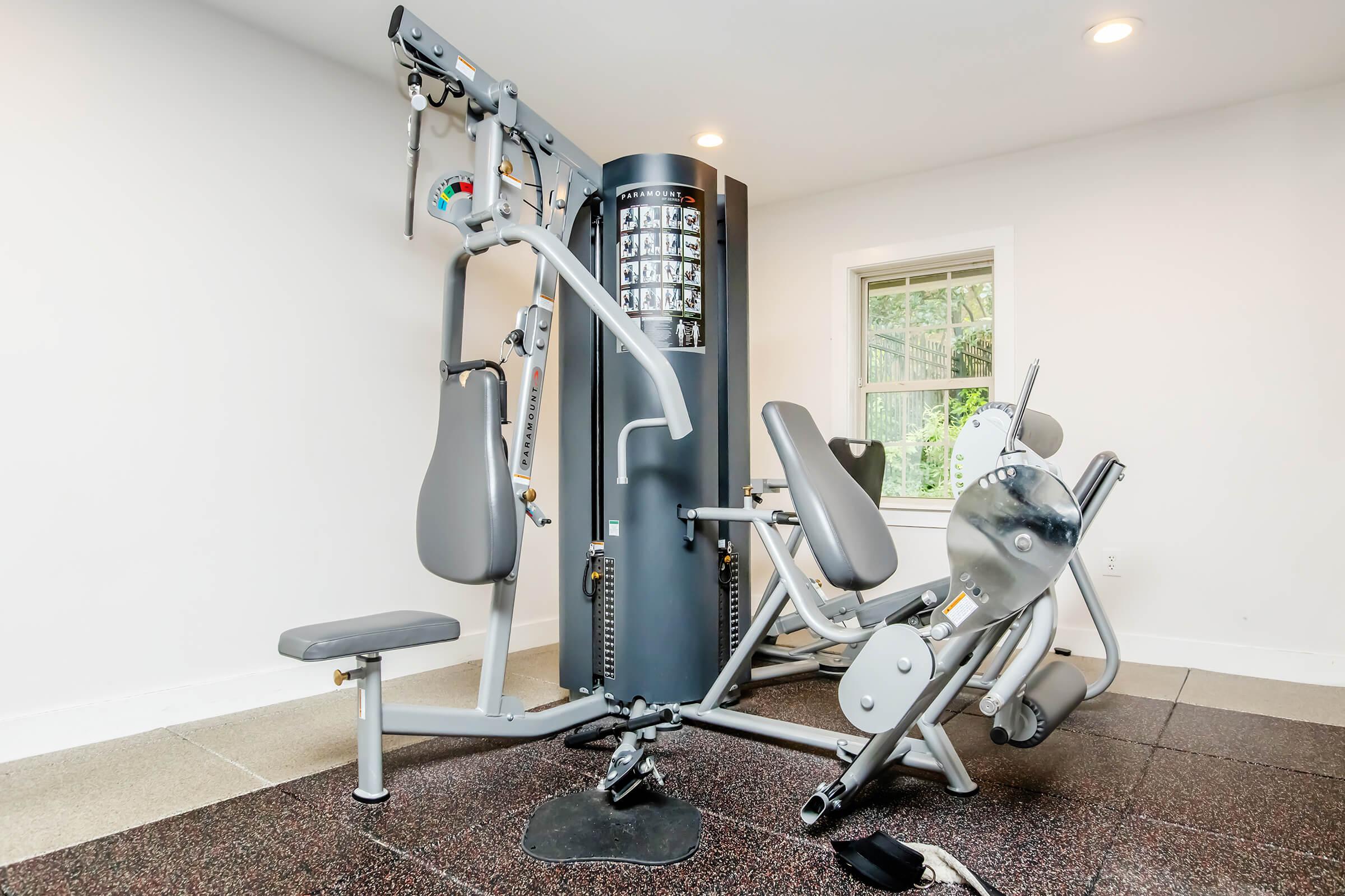 A modern gym with a multi-station exercise machine featuring various attachments for strength training, surrounded by smooth flooring and natural light from a window. The space is clean and organized, highlighting fitness equipment for a home gym setup.