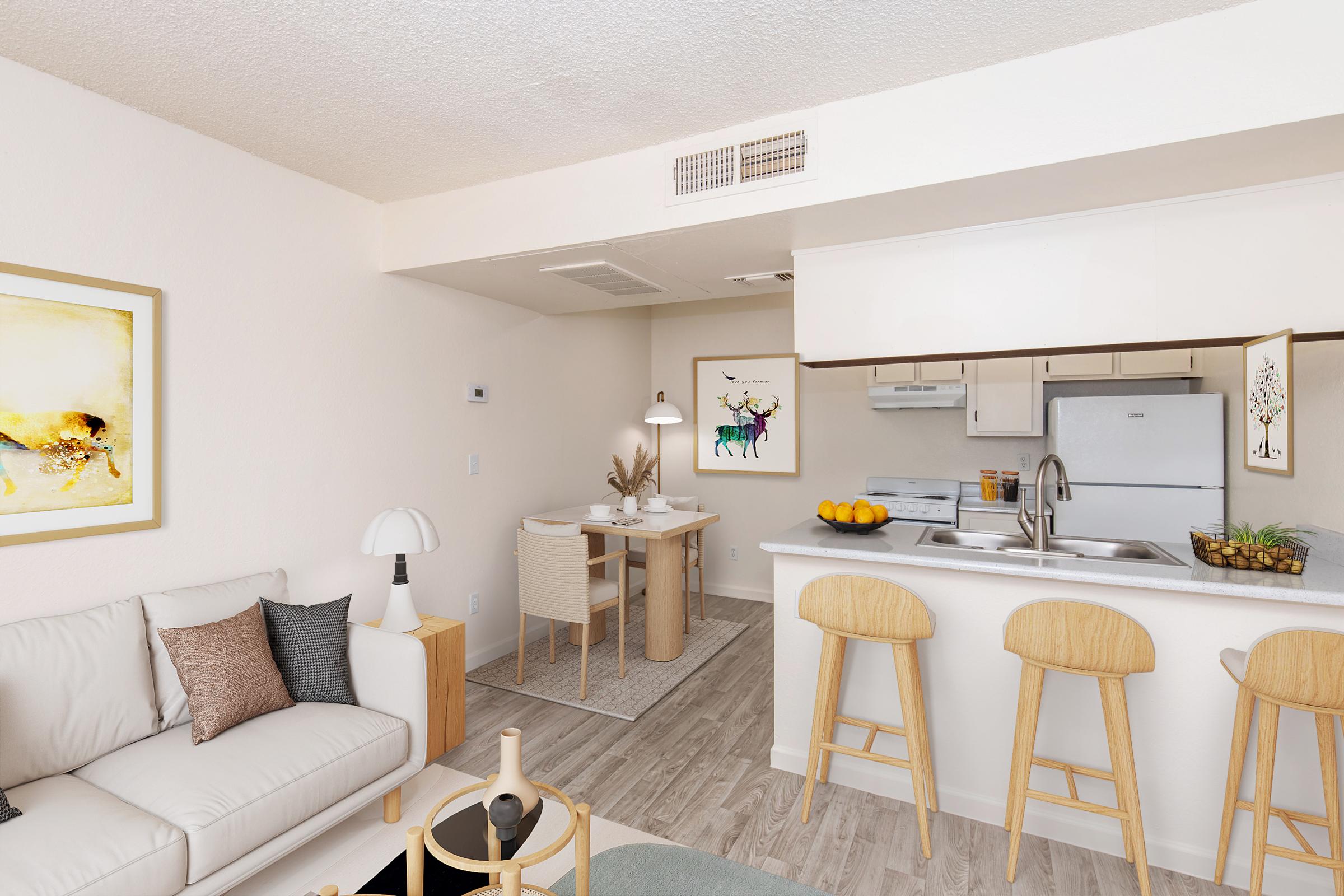 A modern, clean living space featuring a comfortable sofa, a small dining area with a table and chairs, and a kitchen with appliances. The decor includes artwork on the walls, a light color palette, and natural wood elements, creating a bright and inviting atmosphere.