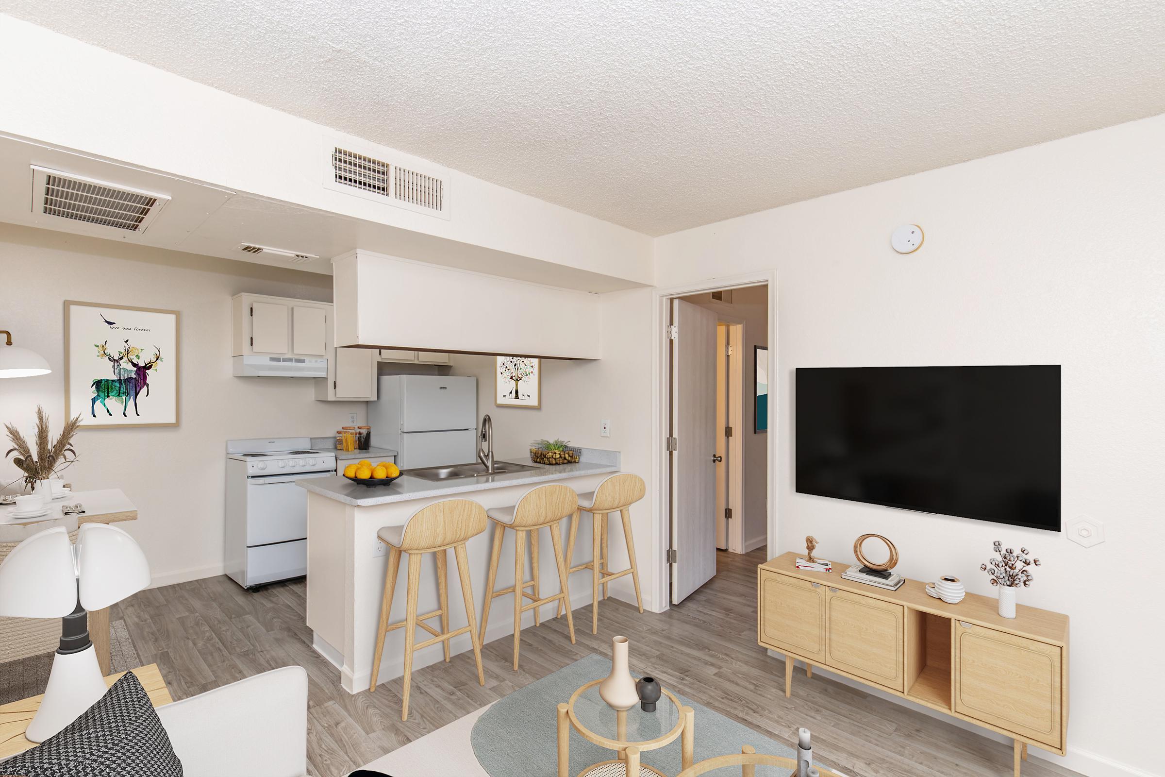 A modern living space featuring a kitchen with white appliances and a small dining area with three barstools. The open layout includes a cozy seating area with decorative items, a TV on a light wooden console, and soft neutral-colored walls, creating a warm and inviting atmosphere.