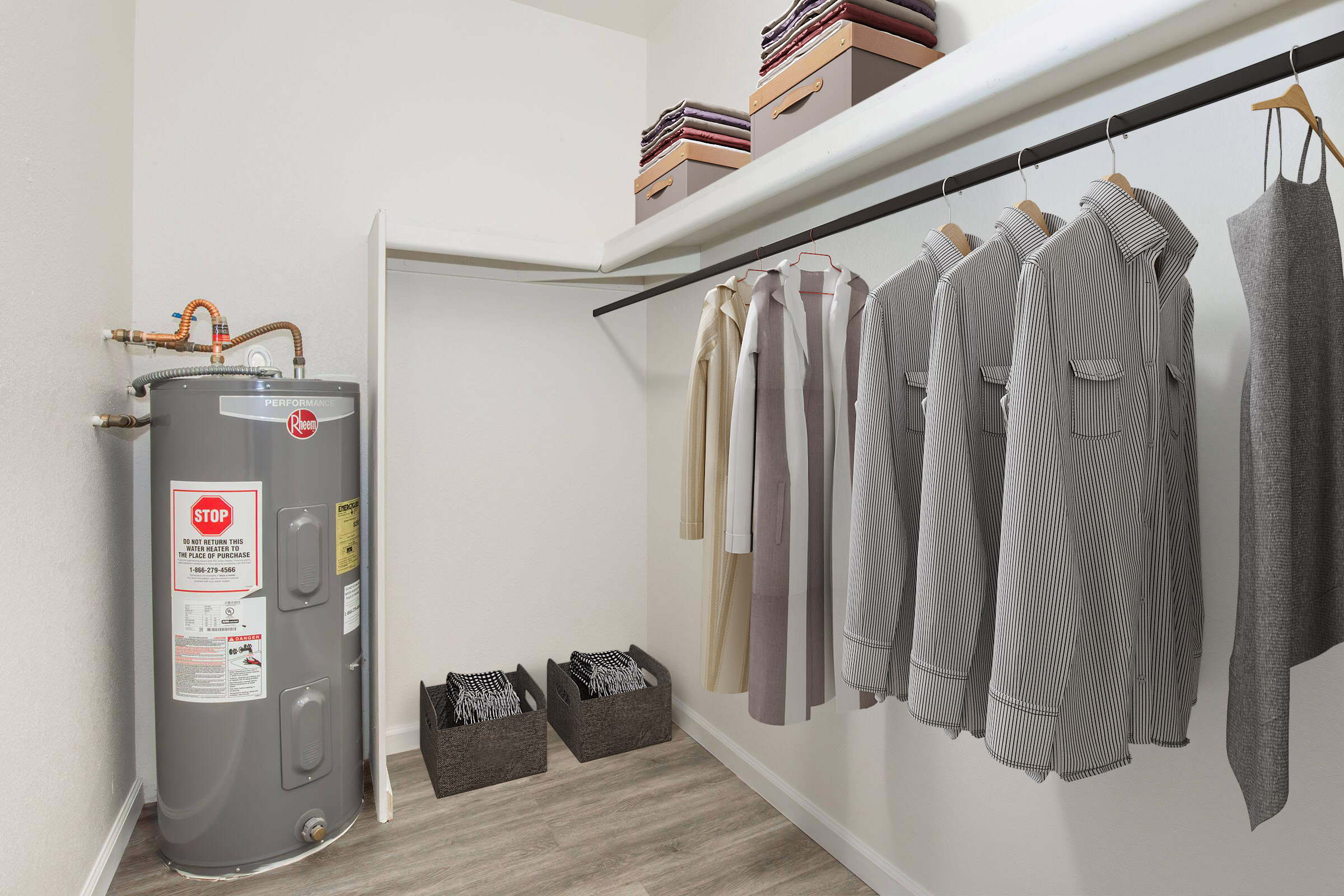 A neatly organized closet featuring a gray water heater against the wall, with several hanging shirts and jackets on a clothing rod. Two storage baskets are placed on the floor, and the closet is well-lit with a clean, modern design.