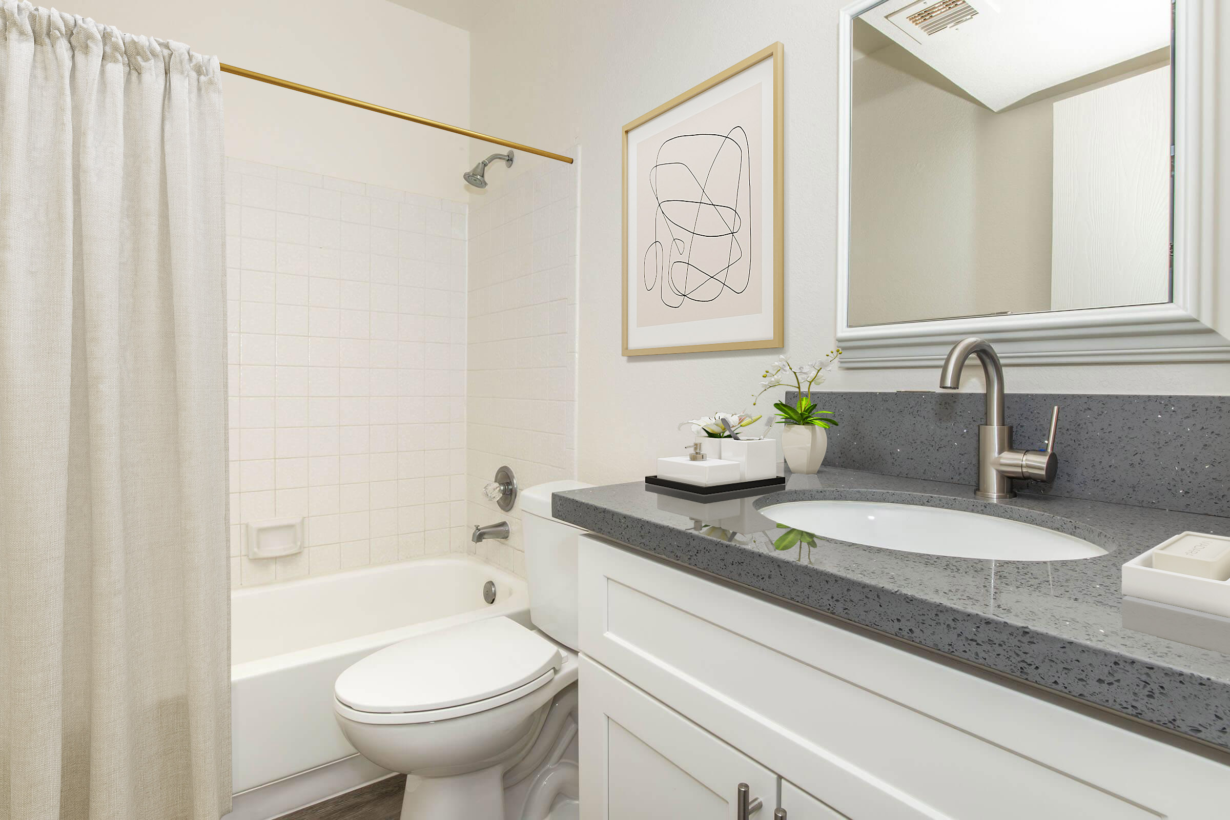 A modern bathroom featuring a white bathtub with a shower curtain, a compact vanity with a dark countertop, and a mirror above the sink. Minimalist decor includes a framed abstract artwork and a small plant on the counter, contributing to a clean and stylish aesthetic.