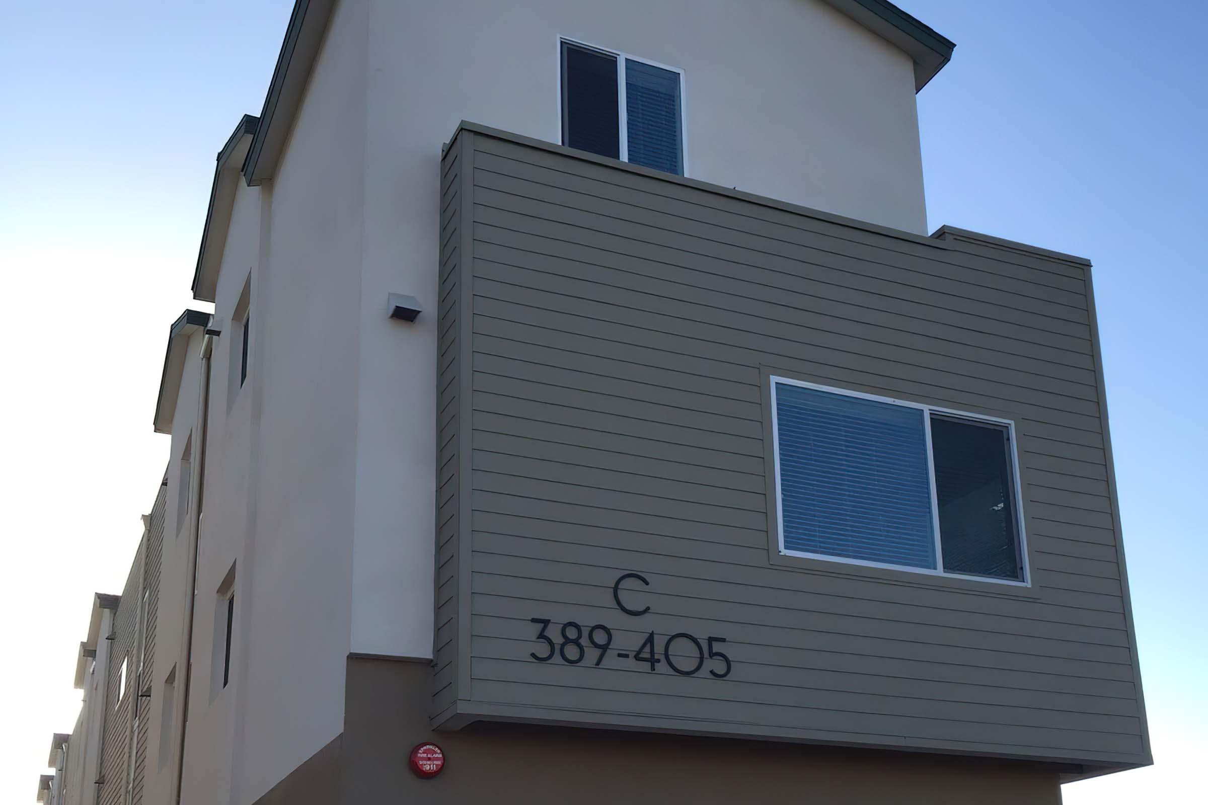Apartment building exterior featuring a light-colored wall with horizontal siding, a large window, and a balcony.