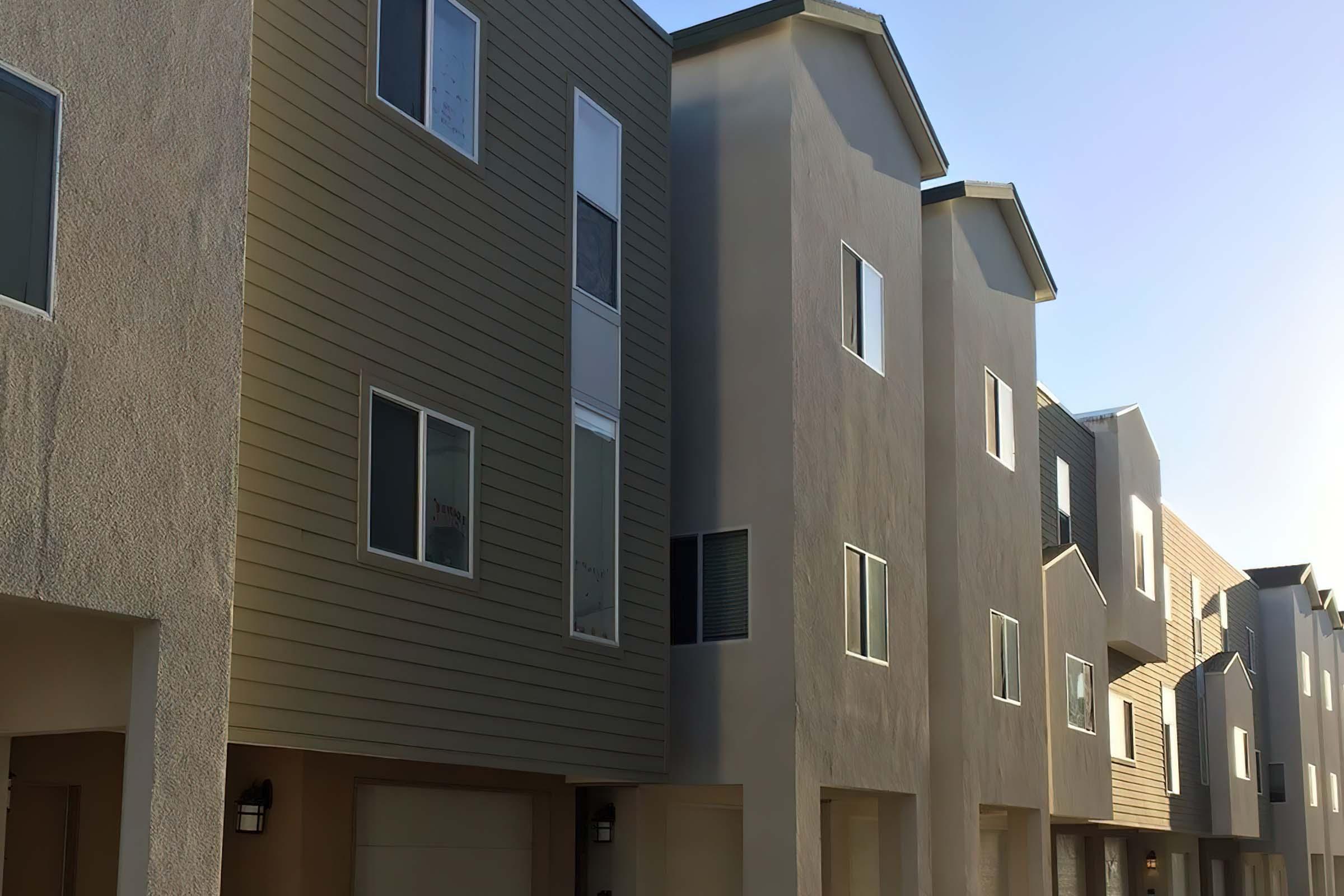 A row of modern townhouse buildings with a mix of beige and olive green siding.
