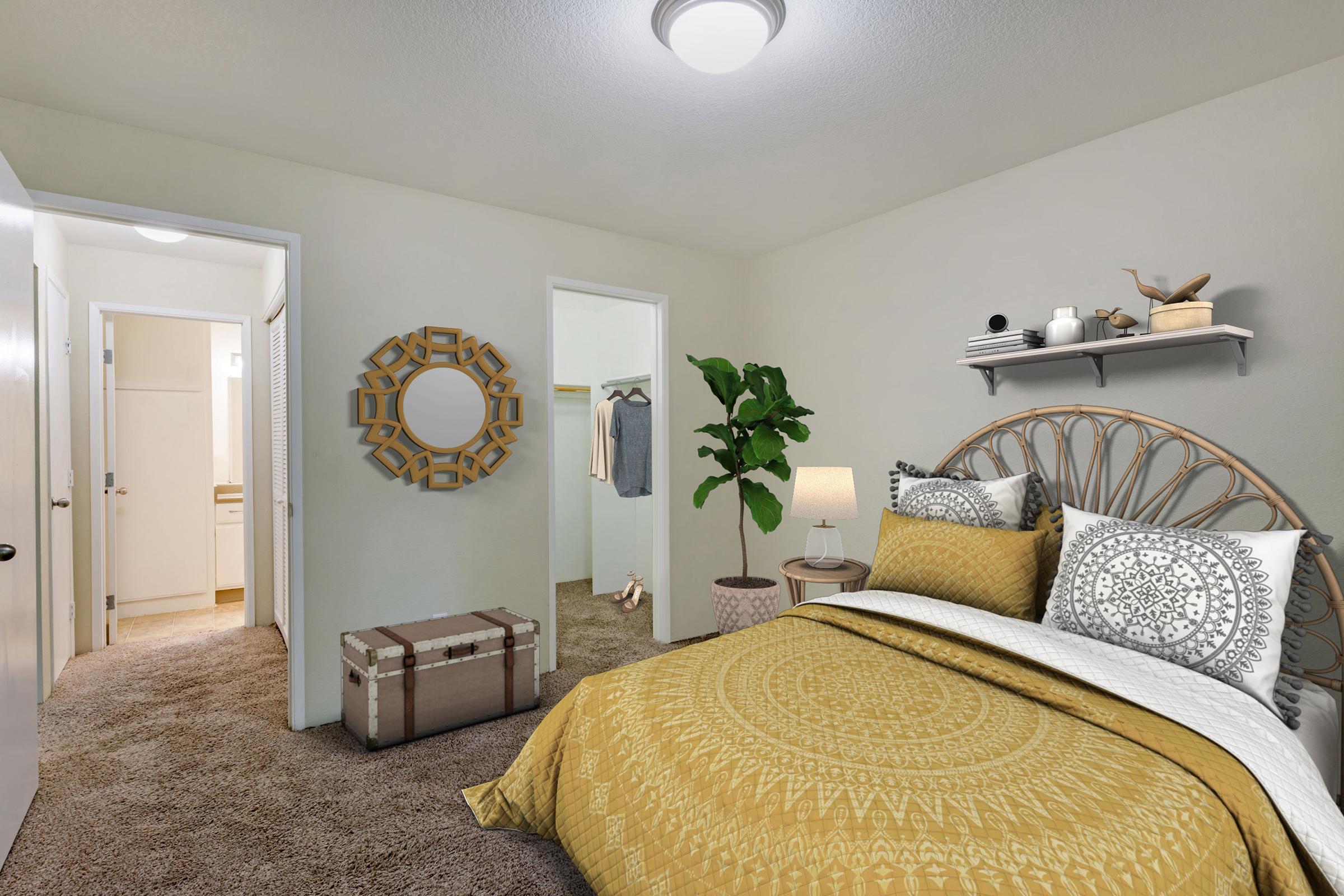A cozy bedroom featuring a bed with a yellow and white patterned duvet, a decorative mirror, and a potted plant.