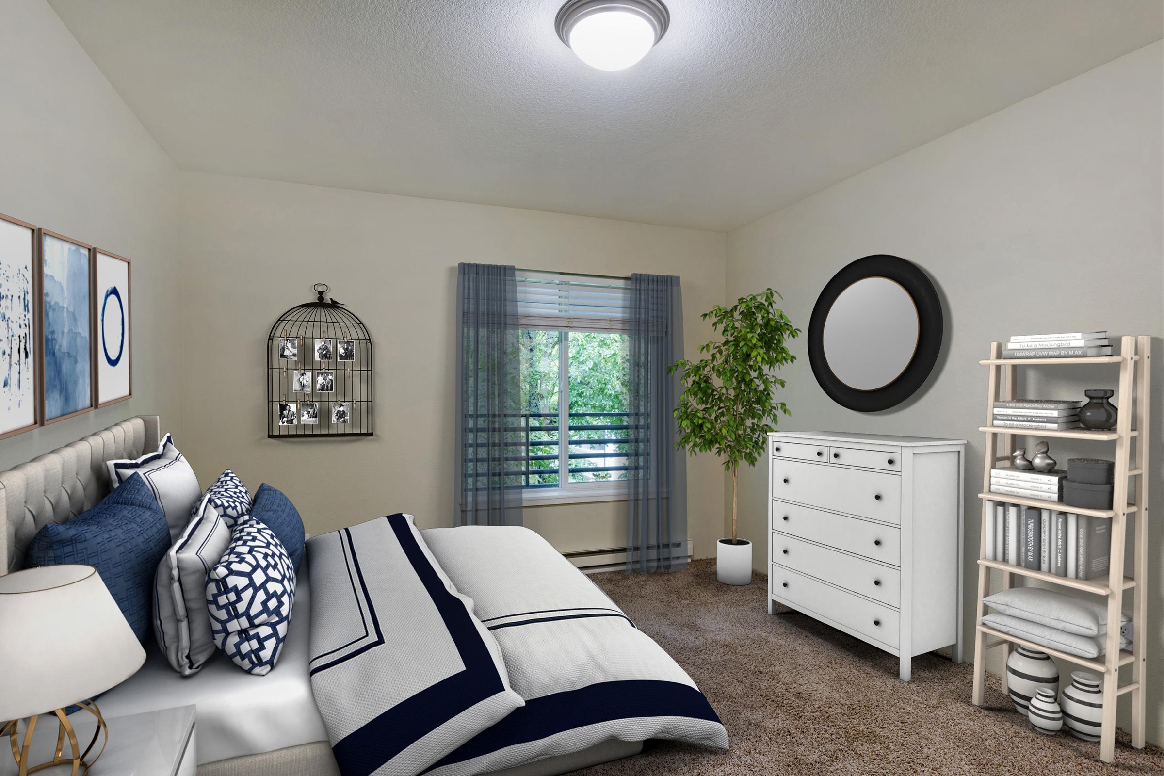 A cozy bedroom featuring a neatly made bed with navy and white pillows, a round mirror on the wall, a white dresser, and a bookshelf. A framed photo display hangs next to a decorative birdcage.