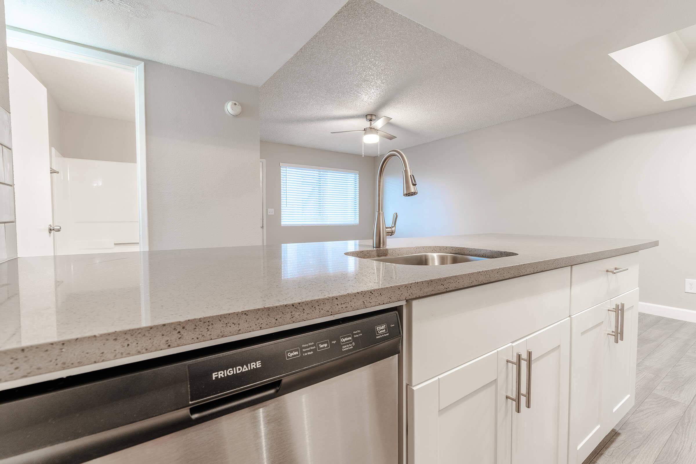 Close up view of kitchen island with grey quartz counter tops and a built in sink and dishwasher