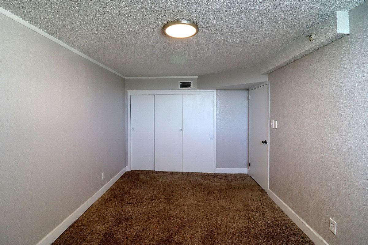 Empty room with gray walls and carpeted floor. A circular ceiling light is mounted above. There are two large white closets on one wall and a door leading to another area on the right. The room has a simple and minimalistic design, with no furniture present.
