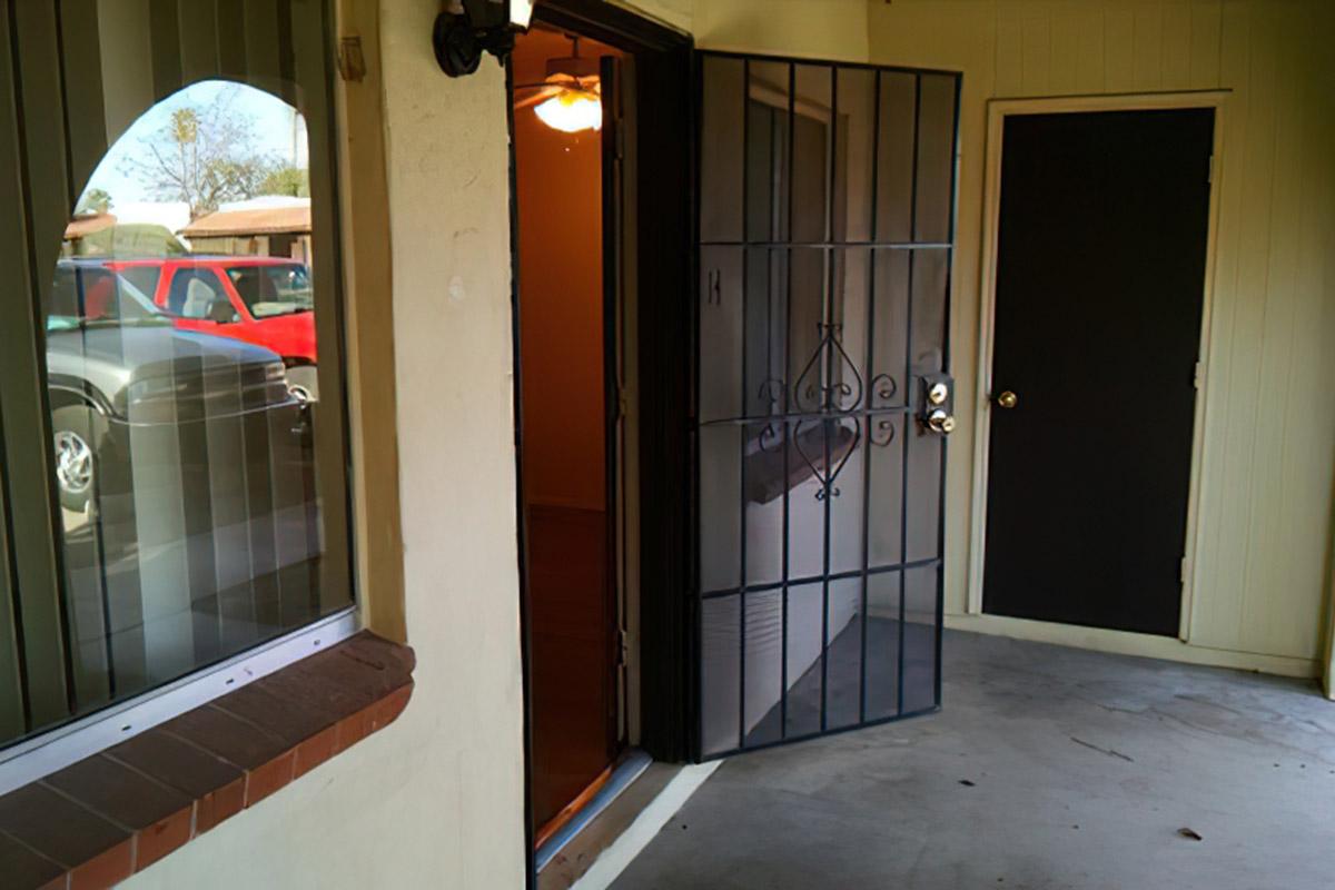 A view of an entrance to a building featuring a partially open security door. The interior is illuminated, and a closed black door is visible to the right. The exterior has a small overhang, and there's a vehicle parked outside, partially visible in the background.