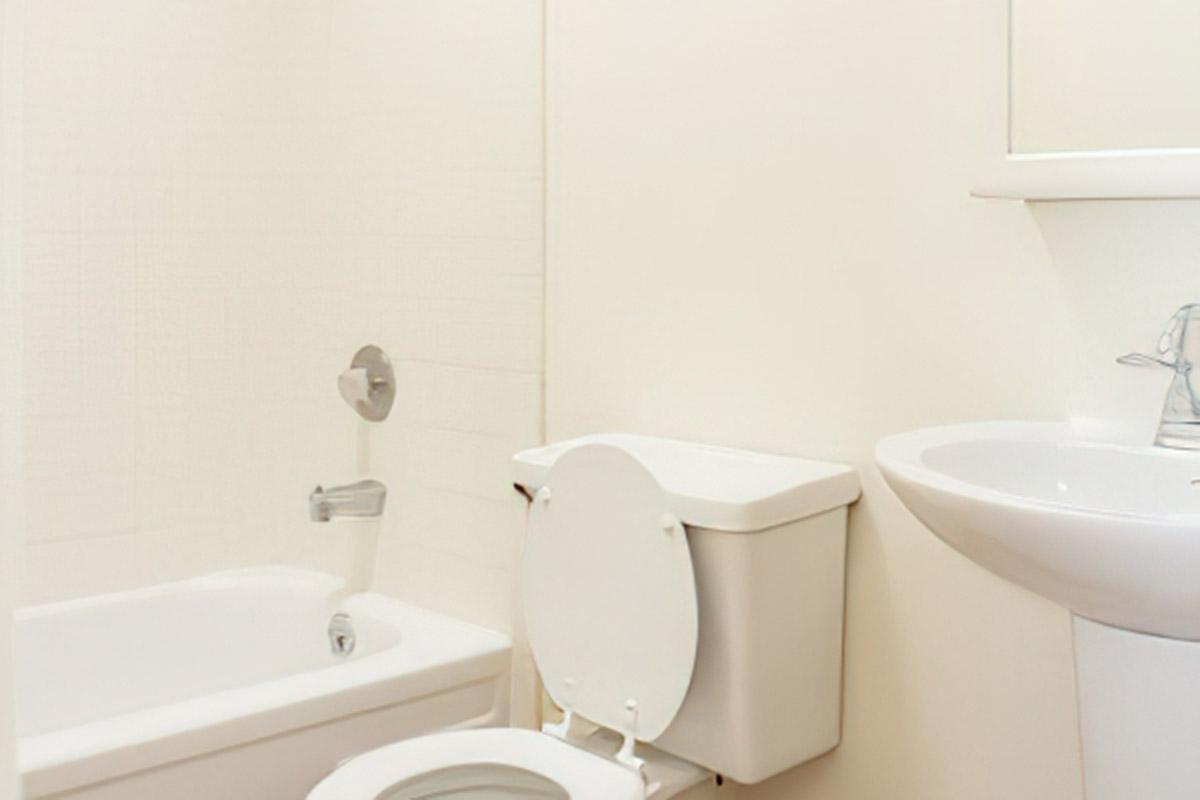 A clean, modern bathroom featuring a white bathtub, a wall-mounted faucet, a toilet, and a pedestal sink. The walls are light-colored, contributing to a bright and airy atmosphere. The design is simple and functional.