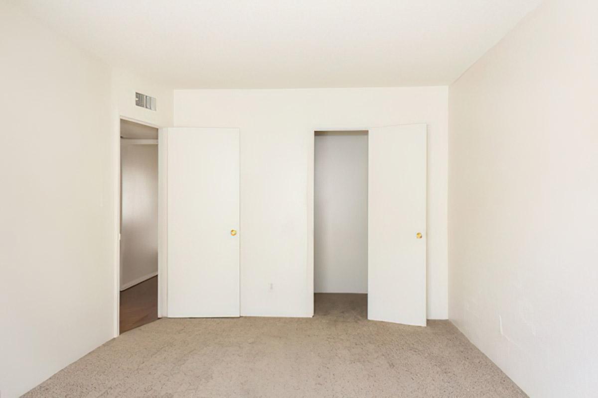Empty room with beige carpet, white walls, and two closed doors on the left and right. The space appears minimalistic and well-lit, suggesting a neutral atmosphere.