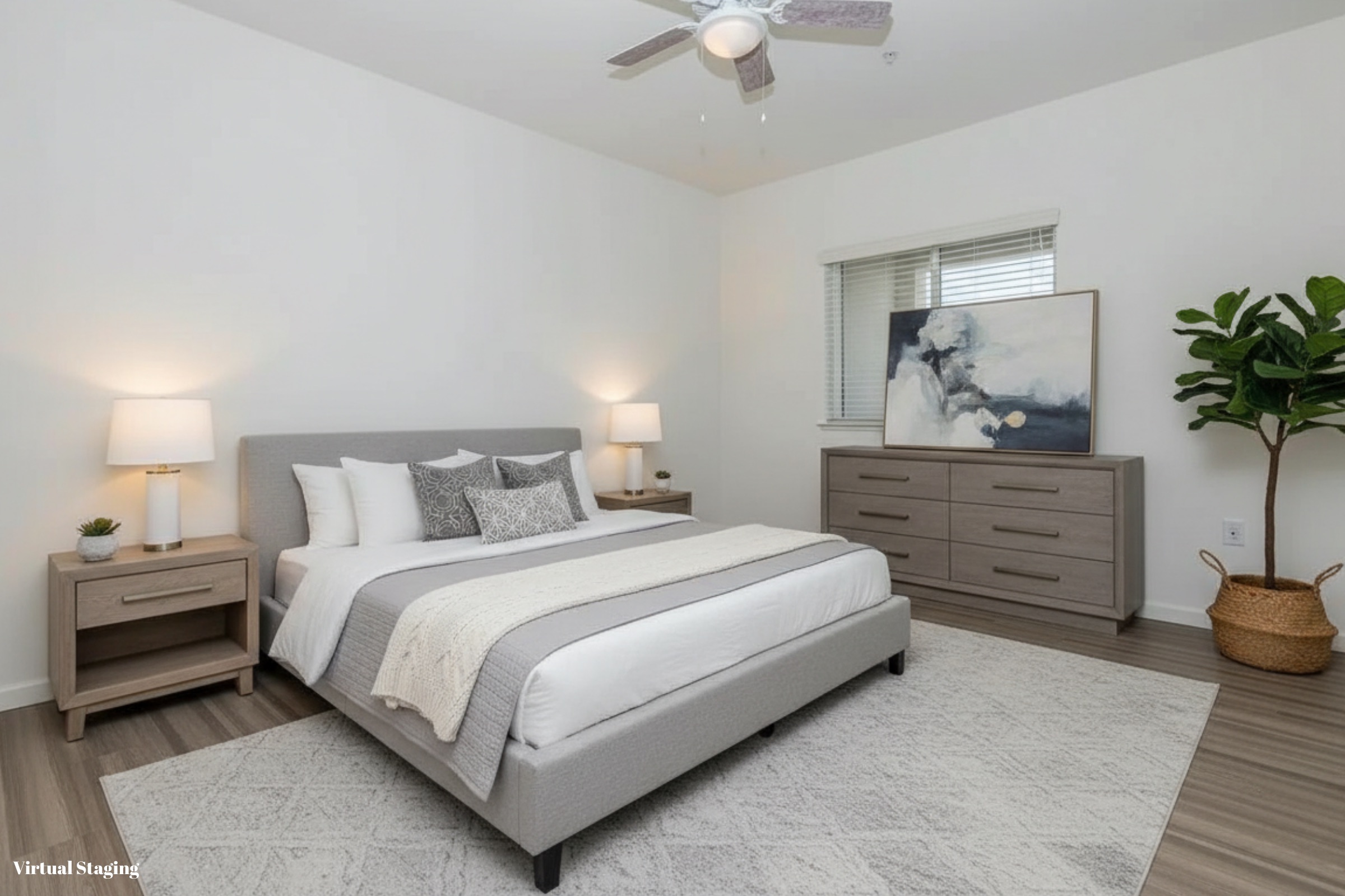 A modern bedroom featuring a gray upholstered bed with decorative pillows, two bedside tables with lamps, a stylish dresser, and a large artwork on the wall. A potted plant adds a touch of greenery, and the space is accented by wooden flooring and soft light from a ceiling fan.