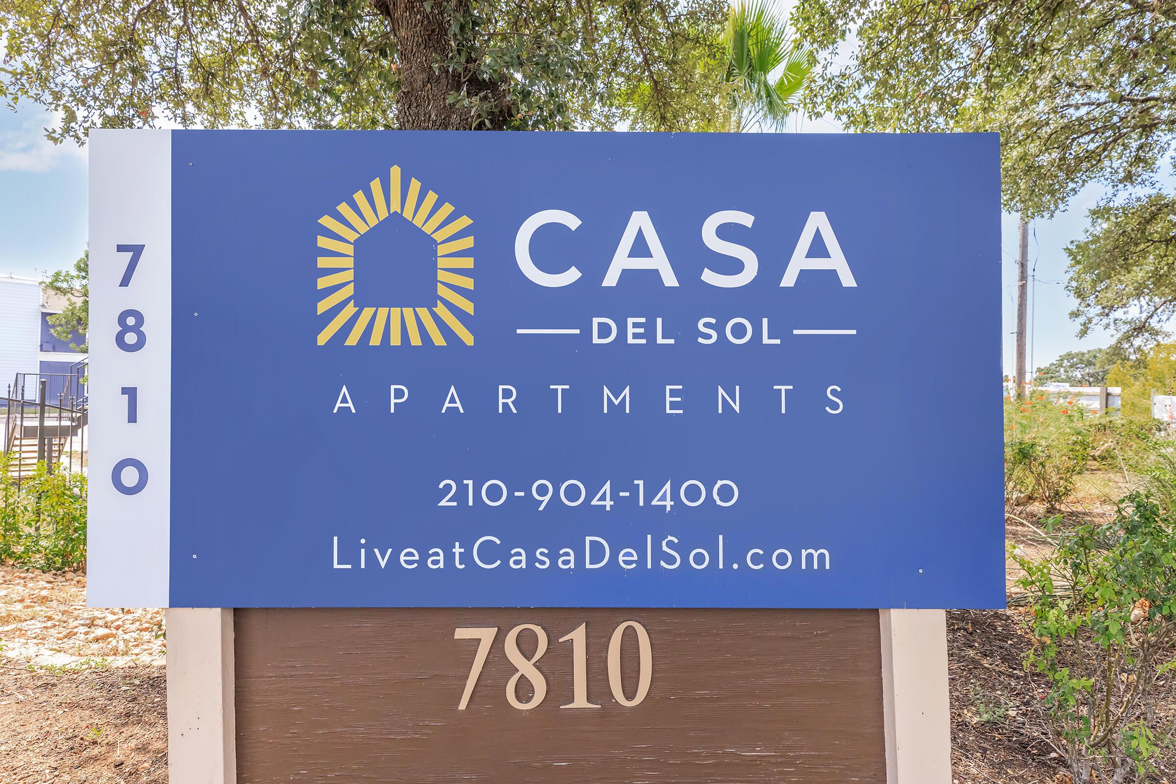 Sign for Casa Del Sol Apartments featuring the name, phone number (210-904-1400), and website (LiveatCasaDelSol.com). Located at 7810, the sign is prominently displayed outdoors with surrounding greenery.